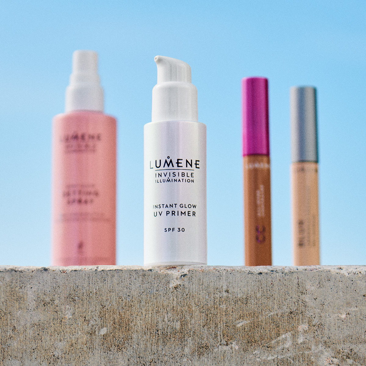 Fyra Lumene hudvårdsprodukter på en betongyta utomhus. Setting spray, UV primer, CC cream och concealer.