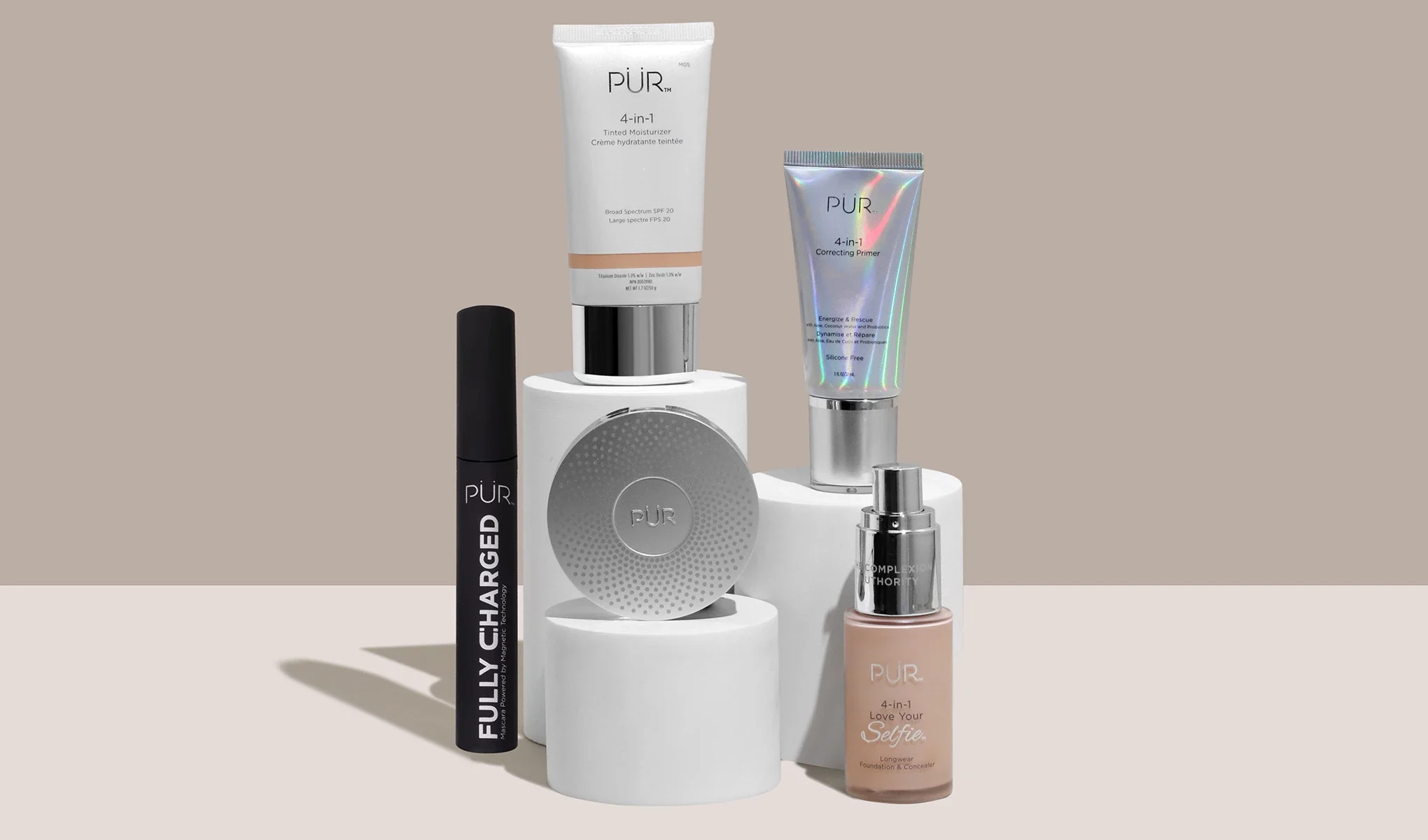 PÜR-produkter, inkludert mascara, primer, fuktighetskrem, foundation og pudder, stilrent presentert på hvite podier mot en beige bakgrunn.