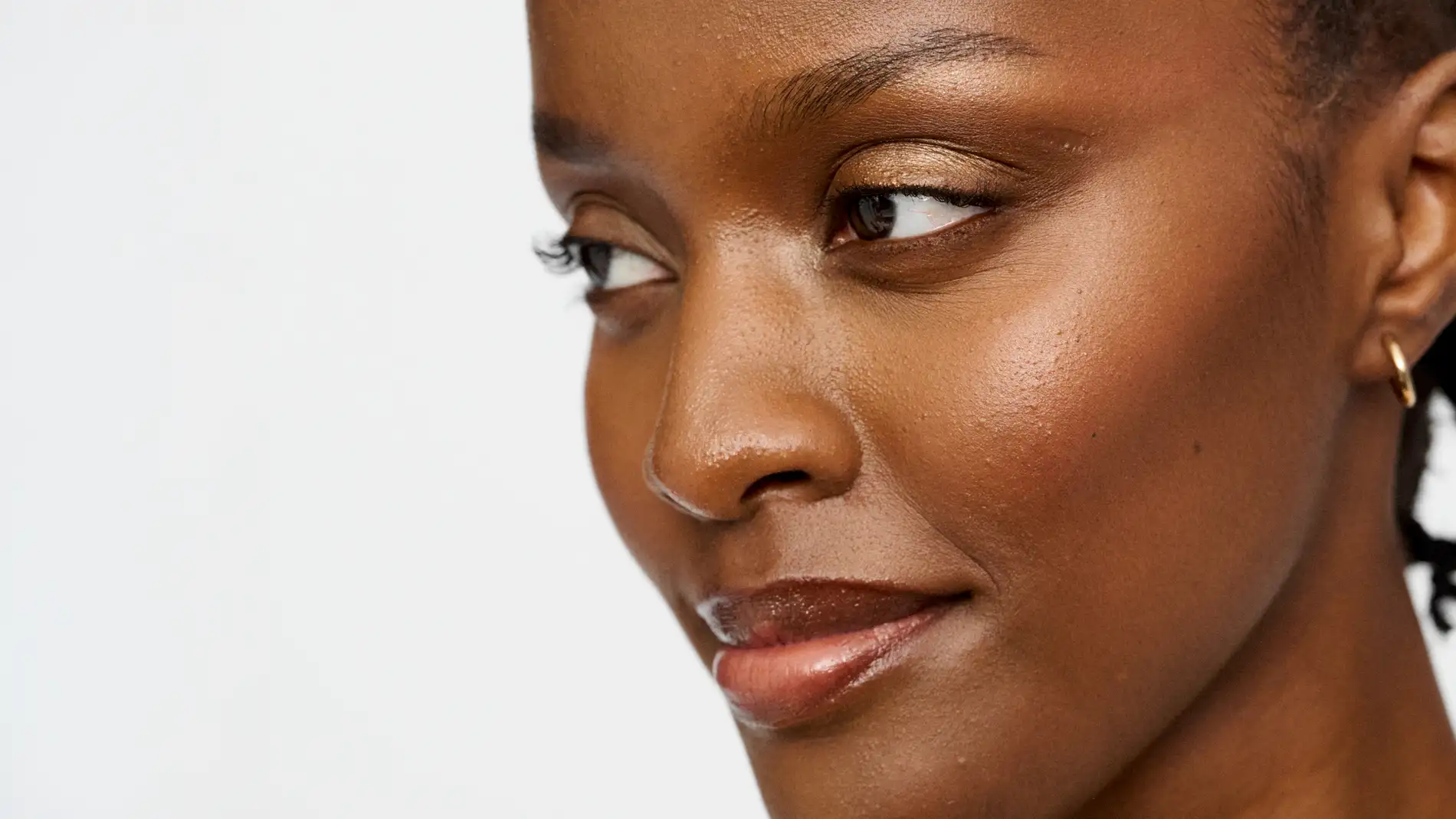 Vakker kvinne med sminke som ser til siden mot hvit bakgrunn.