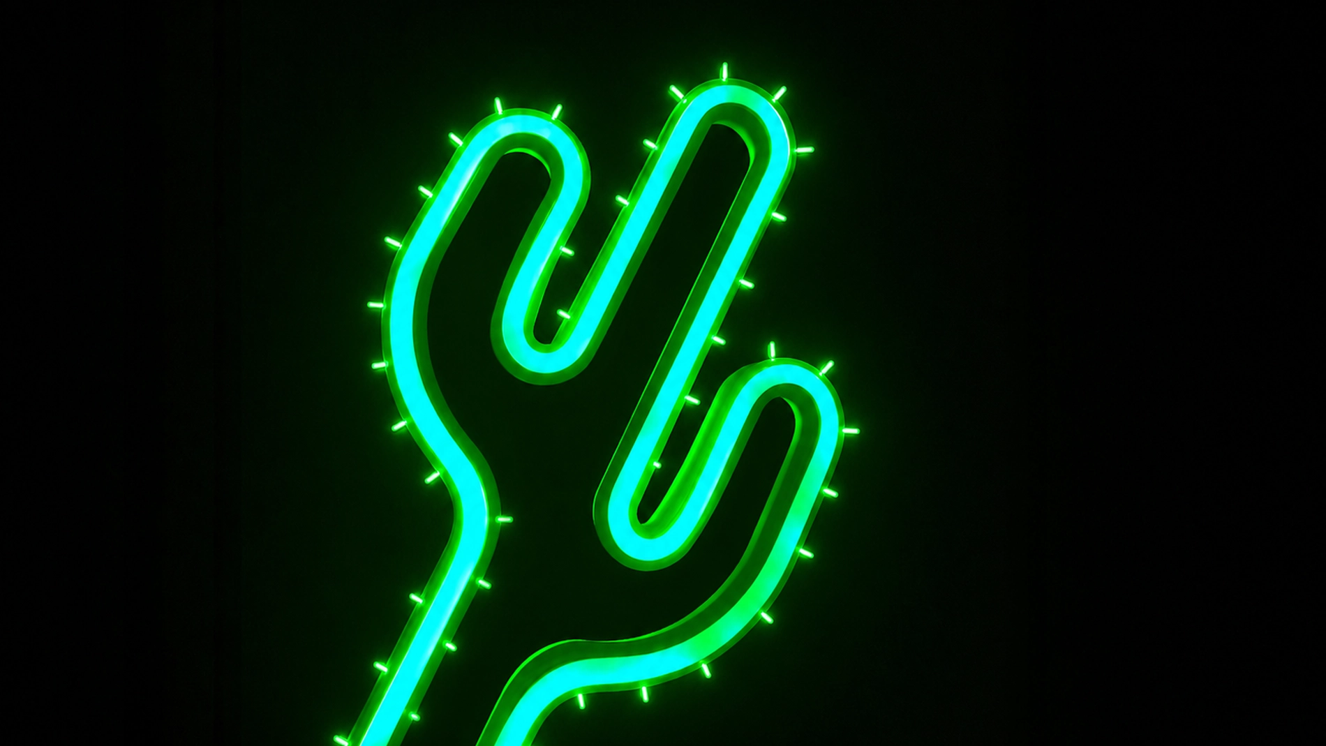 Neonskylt formad som en grön kaktus med turkosa detaljer mot svart bakgrund. Den lysande dekorationen har små upplysta taggar längs kanterna och skapar en modern och grafisk känsla.