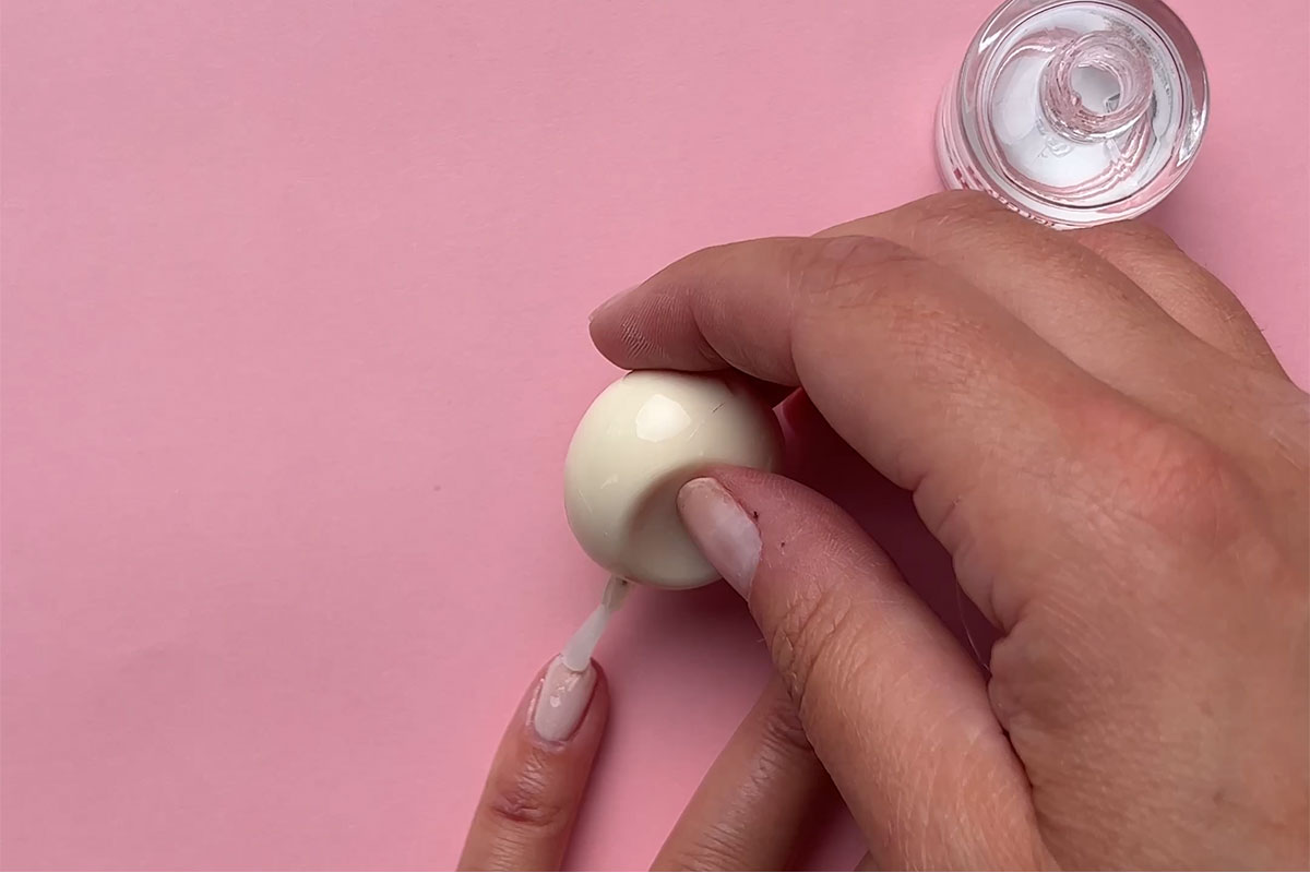 Topplakk som påføres en lillefinger med rosa bakgrunn.
