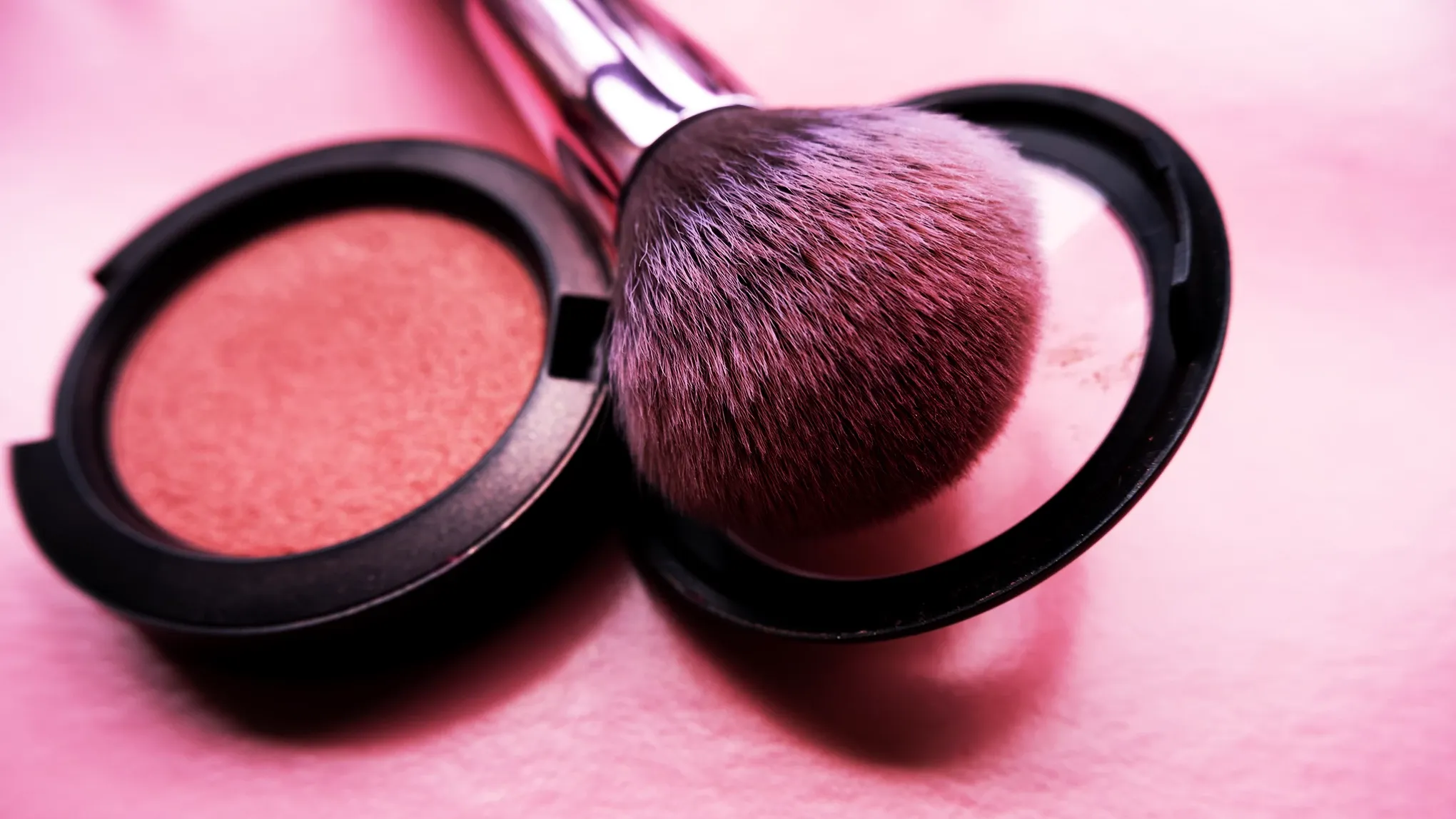 Sminkborste med rosa puder placerad i en öppen Rouge på en rosa yta