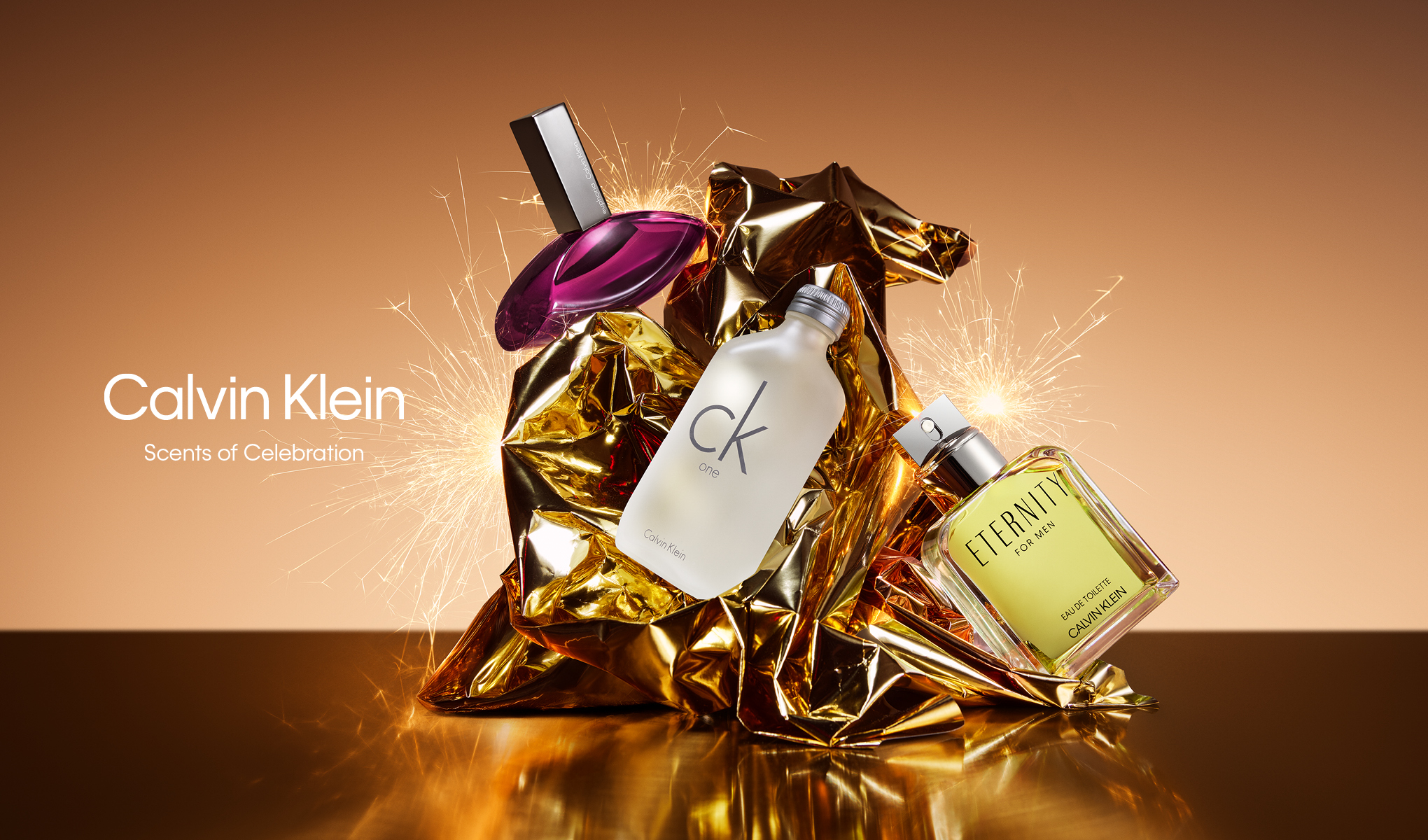 Kolme Calvin Klein -hajuvesipulloa kultaisessa käärepaperissa, ympärillään kipinöitä. Teksti "Calvin Klein" ja "Scents of Celebration" vasemmassa alakulmassa.