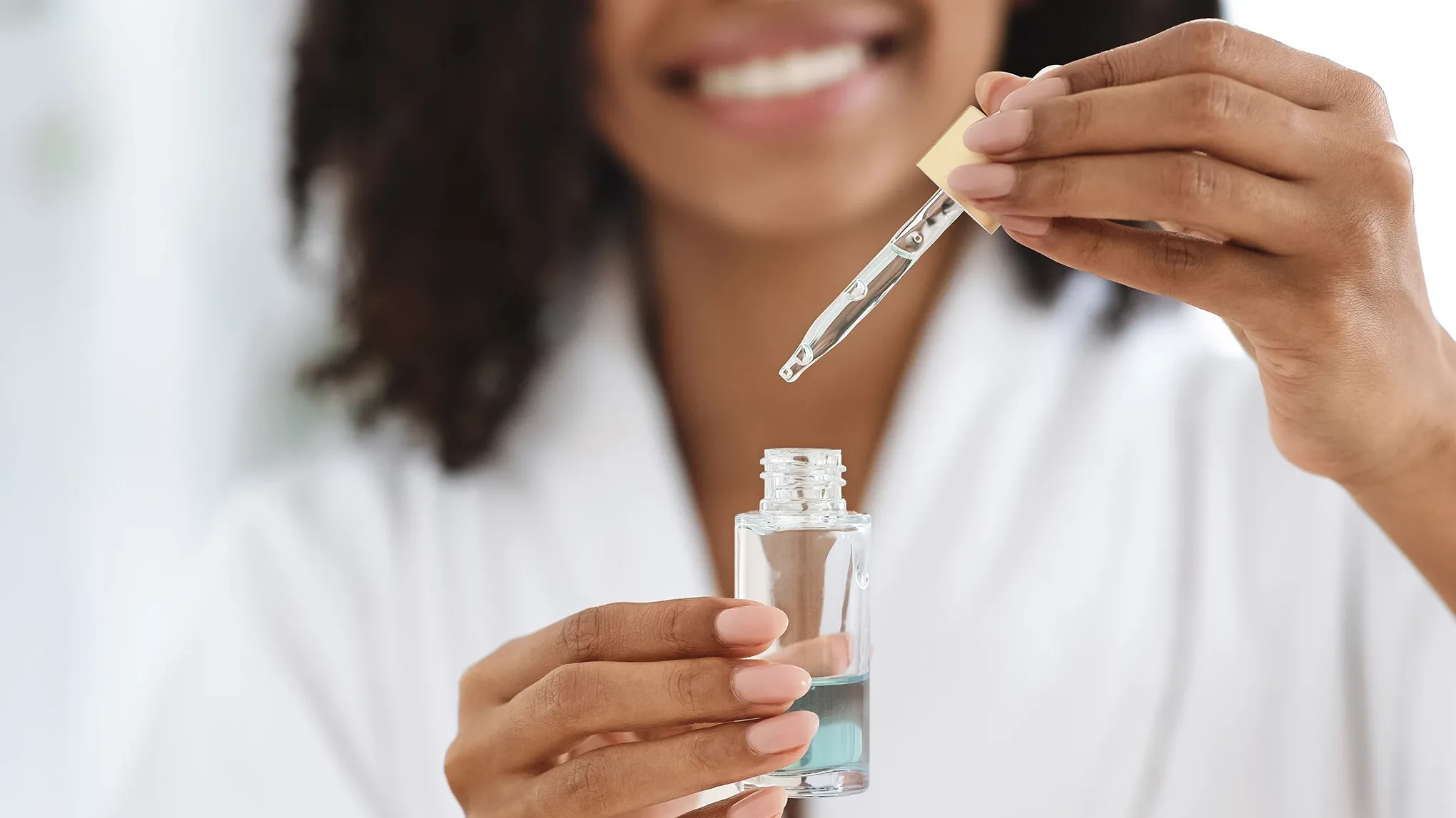 En person holder en pipette og en flaske med hudpleieprodukt.