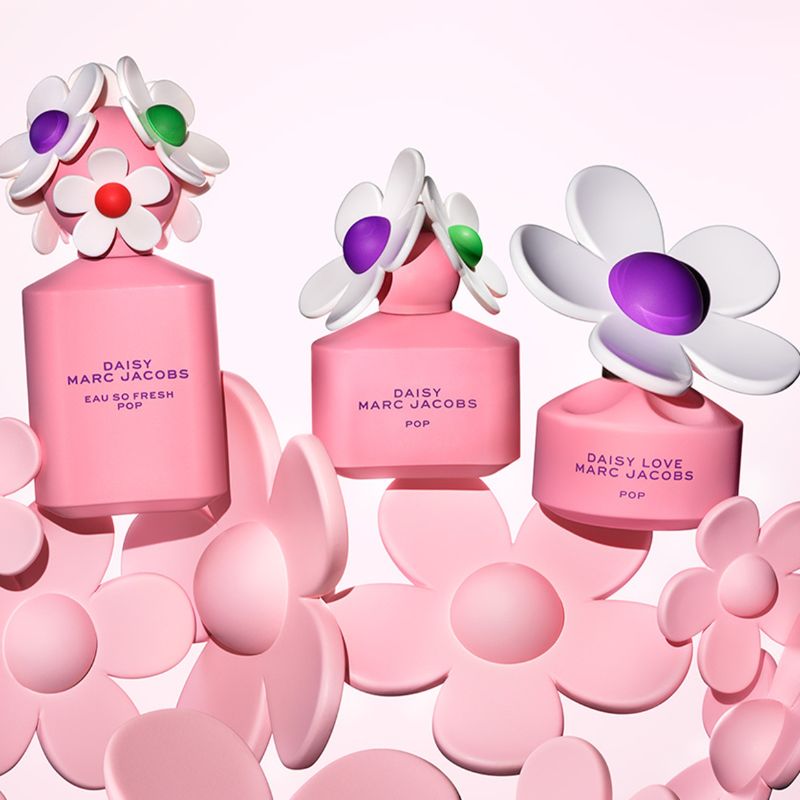 Tre rosa parfymeflasker fra Marc Jacobs' «Daisy Pop»-kolleksjon med blomsterformede hetter i ulike farger. Flaskene er omgitt av rosa blomster mot en lys rosa bakgrunn.