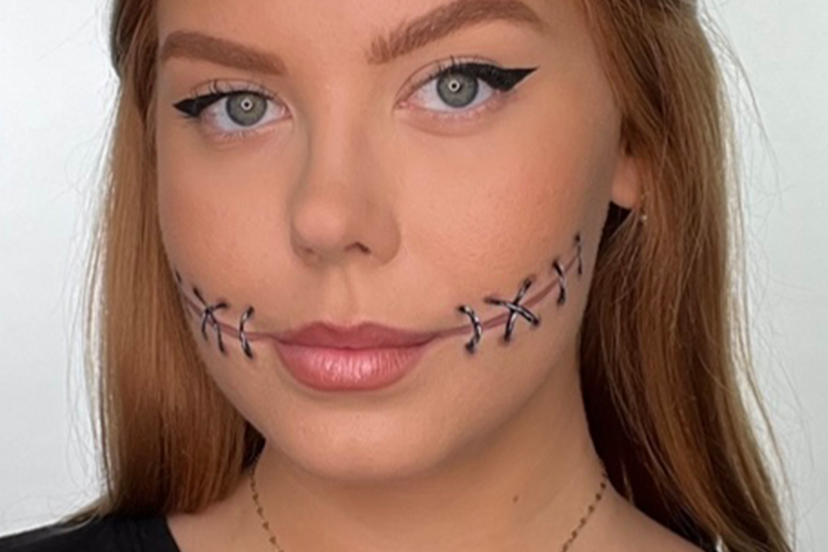 Nainen, jolla on tikkimäinen meikki poskissa ja siipimäinen eyeliner.