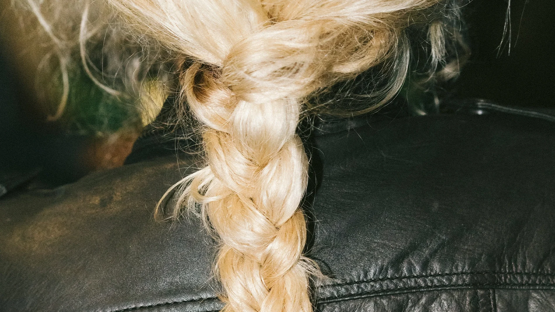 Nærbilde av en flette i lyst blondt hår over en svart skinnjakke, med fokus på hårstruktur og styling for hårpleie.