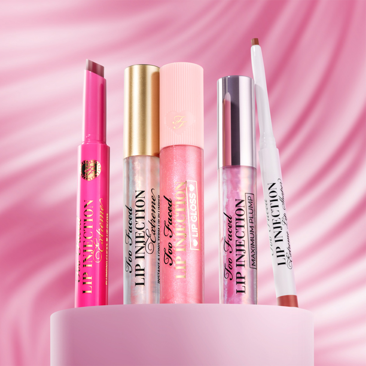 Too Faced-leppeprodukter foran rosa bakgrunn, inkludert lipglosser og lipliner.