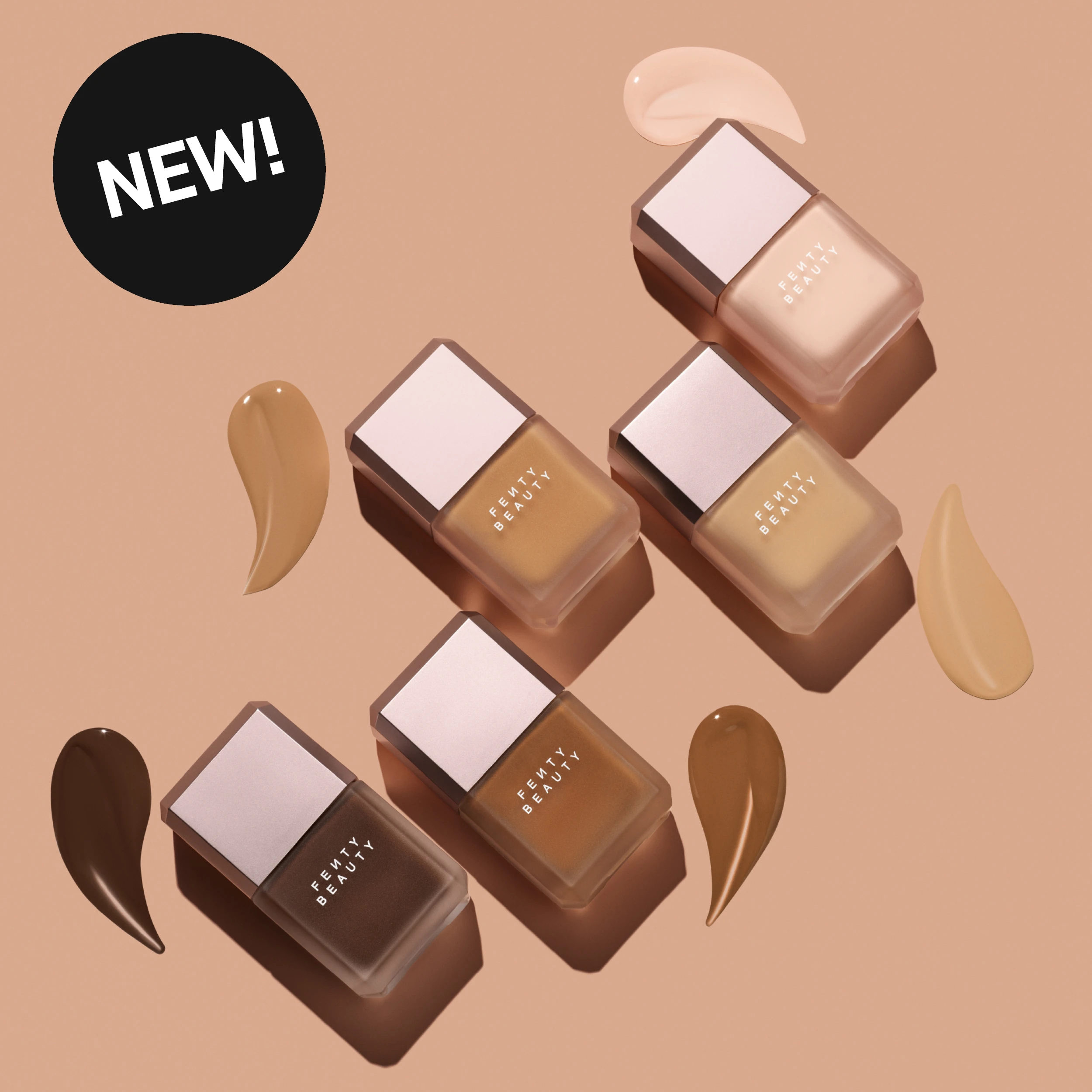 NEW! Viisi Fenty Beauty -foundationpulloa eri sävyissä vaaleasta beigestä tummanruskeaan sekä yhteensopivia foundation-pisaroita lämpimän beigellä taustalla.