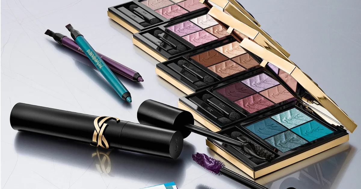 Yves Saint Laurent-sminkeprodukter arrangert på lys bakgrunn. Fire åpne øyenskyggepaletter med applikatorer vises i blå, lilla, rosa og brune nyanser sammen med to eyelinerpenner i turkis og lilla med YSL-logo samt svart mascara med gullfarget YSL-detalj.