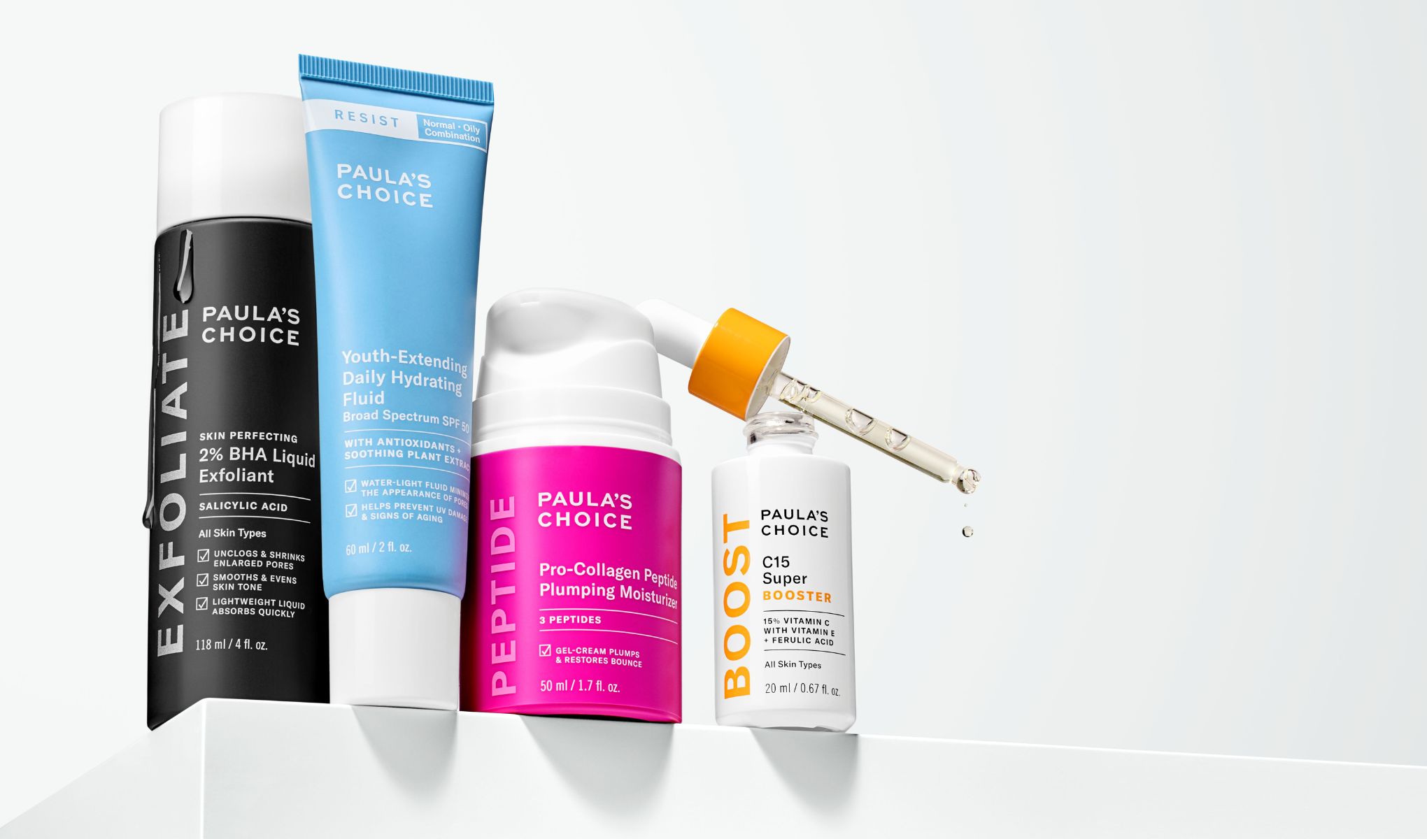 Paula's Choice - Fire hudpleieprodukter står på en hvit overflate. En svart flaske, en blå tube, en rosa pumpeflaske og en hvit flaske med pipette.