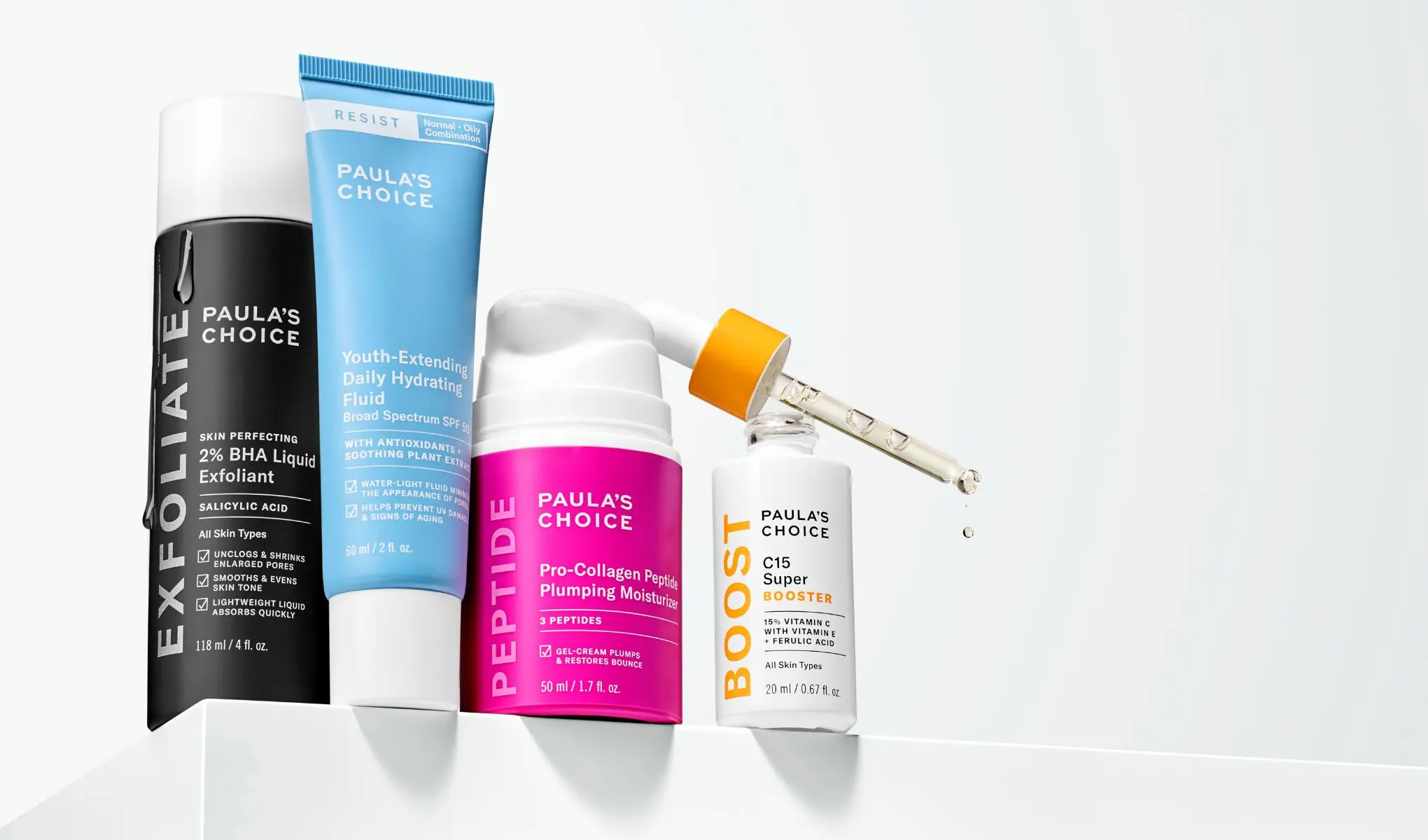 Paula's Choice - Fire hudpleieprodukter står på en hvit overflate. En svart flaske, en blå tube, en rosa pumpeflaske og en hvit flaske med pipette.