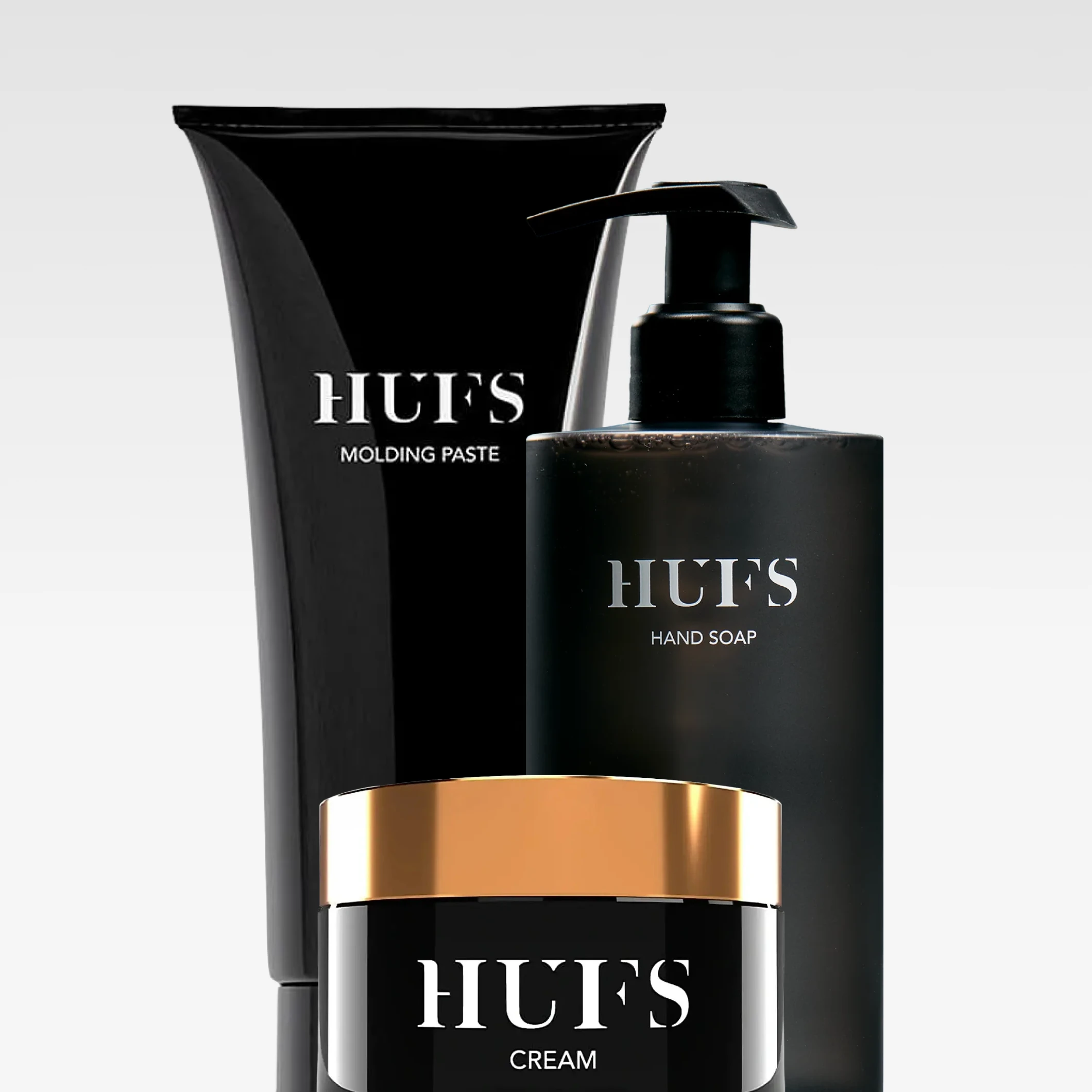 Tre produkter från Hufs: en tub märkt “HUFS MOLDING PASTE”, en pumpflaska “HUFS HAND SOAP” och en burk “HUFS CREAM”. Förpackningarna är svarta med vit text och guldfärgat lock på burken.