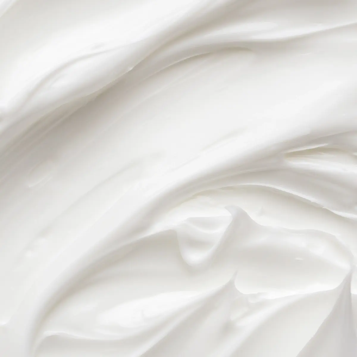 Närbild av vit hudvårdskräm med mjuk, krämig textur och glansiga svep som visar produktens konsistens, lämplig för ansiktskräm eller body lotion.