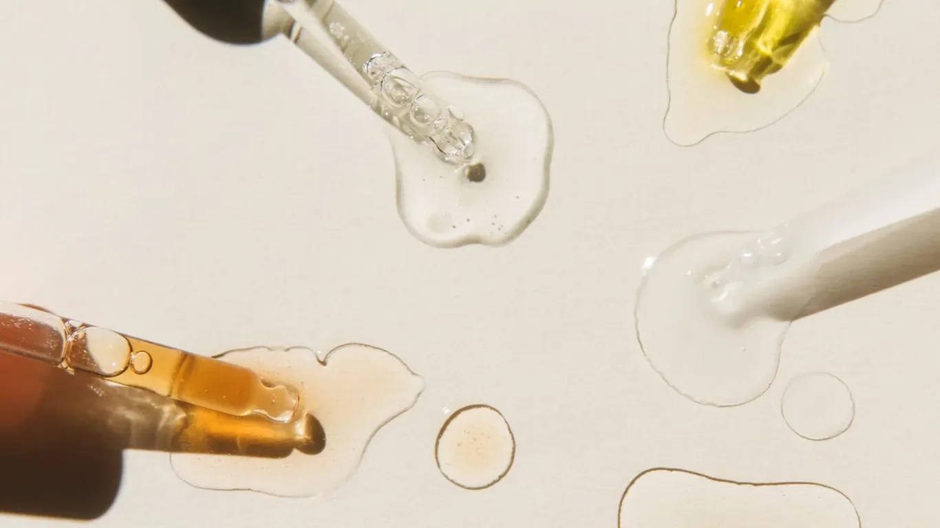 Olika pipetter med serum för hudvård med olikfärgade vätskor och texturer på en ljus yta.