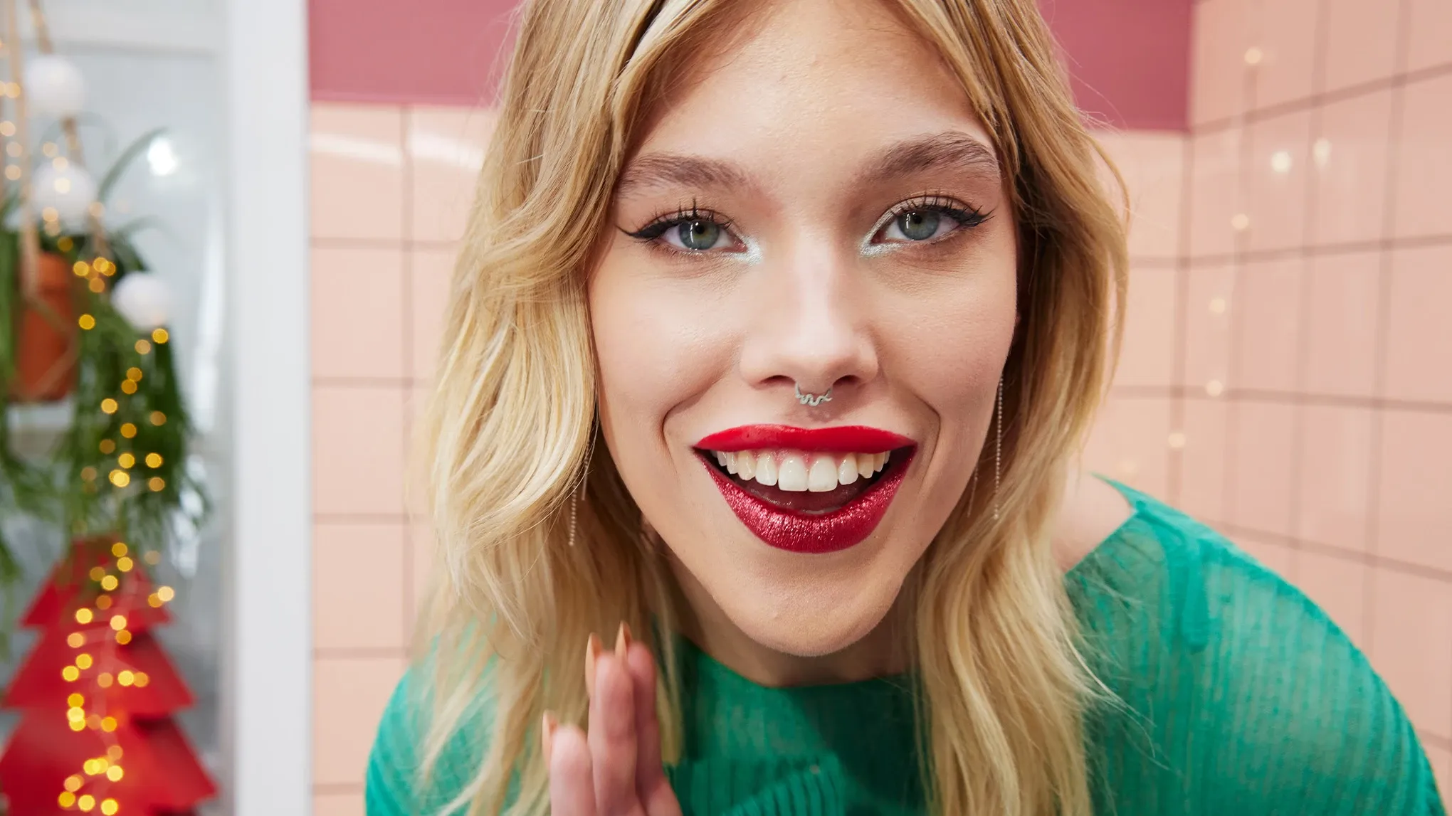 Smilende kvinne med glitrende rød leppestift og eyeliner, iført grønn topp.