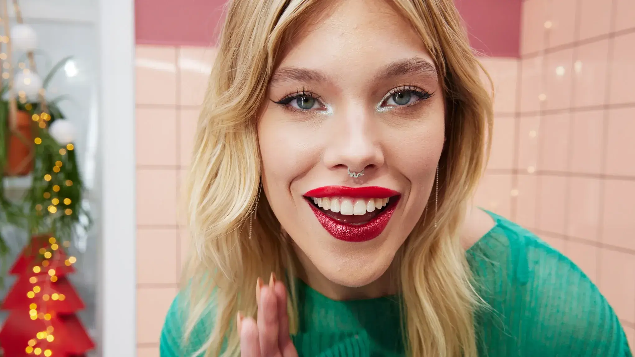 Smilende kvinne med glitrende rød leppestift og eyeliner, iført grønn topp.
