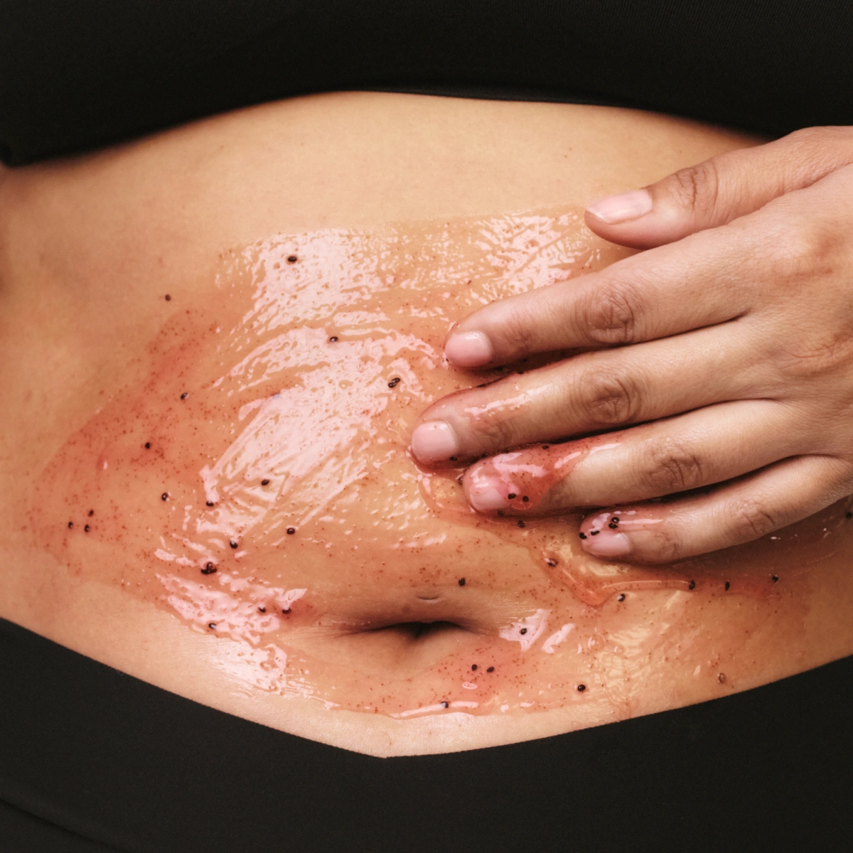 Käsi levittää vartalokuorintaa, jossa näkyy rakeita, vatsan alueelle.