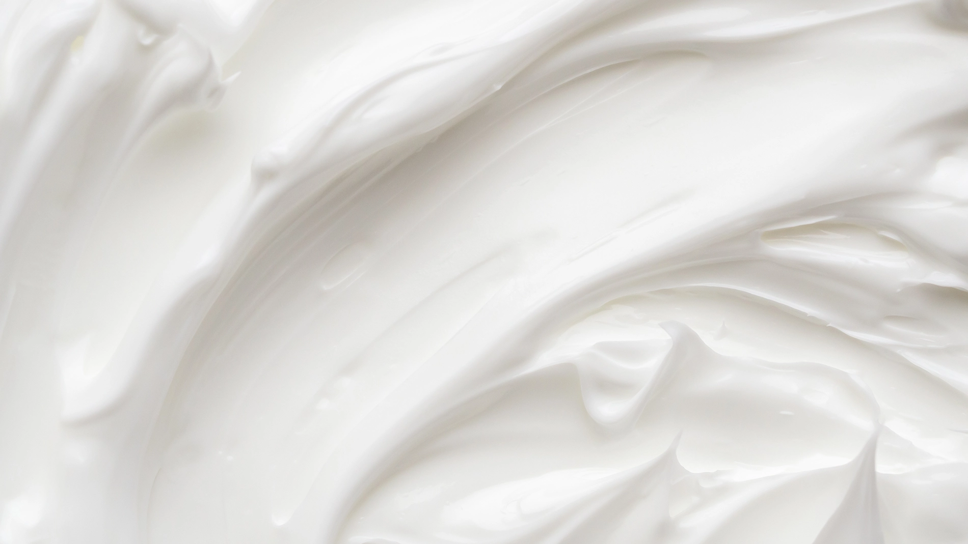 Nærbilde av hvit hudpleiekrem med myk, kremet tekstur og glatte bevegelser som fremhever produktets konsistens, egnet for ansiktskrem eller body lotion.