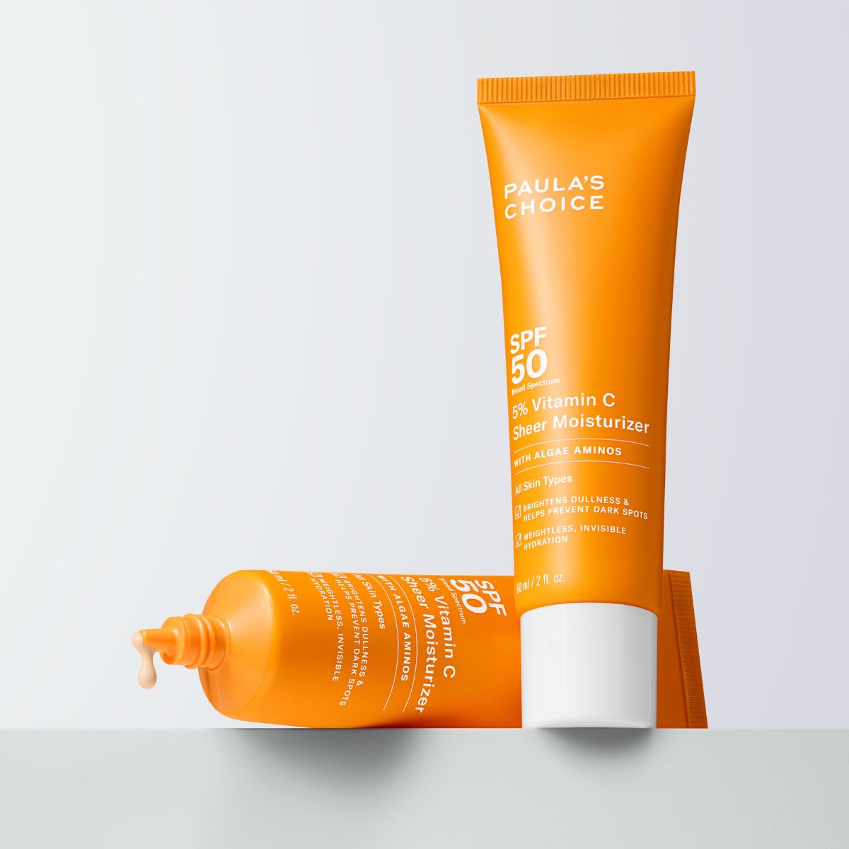 Paula's Choice - Kaksi oranssia tuubia SPF 50 -aurinkosuojalla ja 5% C-vitamiinilla. Yksi tuubi makaa vaakatasossa ja toinen seisoo pystyasennossa.