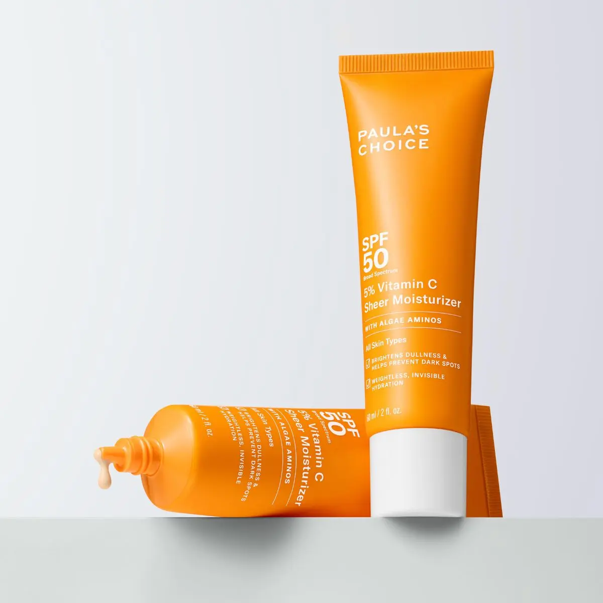 Paula's Choice - Två orange tuber med SPF 50 solskydd och 5% vitamin C. En tub ligger horisontellt och den andra står vertikalt.