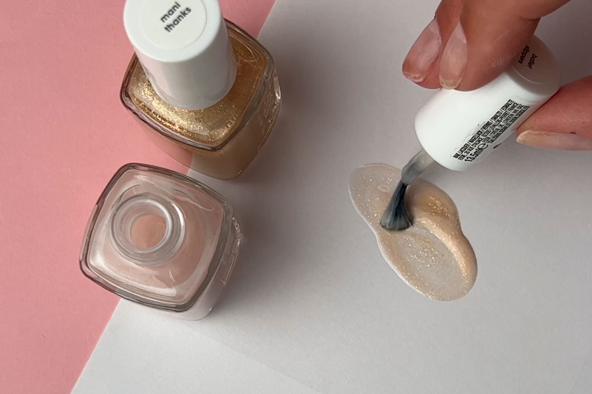 Nagellack som målas på ett vitt papper med två nagellacksprodukter intill aen rosa bakgrund.