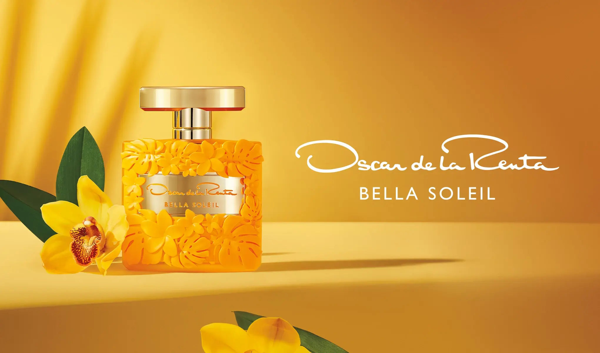 Bildet viser en gul parfymeflaske fra Oscar de la Renta med navnet "Bella Soleil" på en gul bakgrunn, dekorert med blomster. Ved siden av flasken er det en gul blomst med grønne blader.
