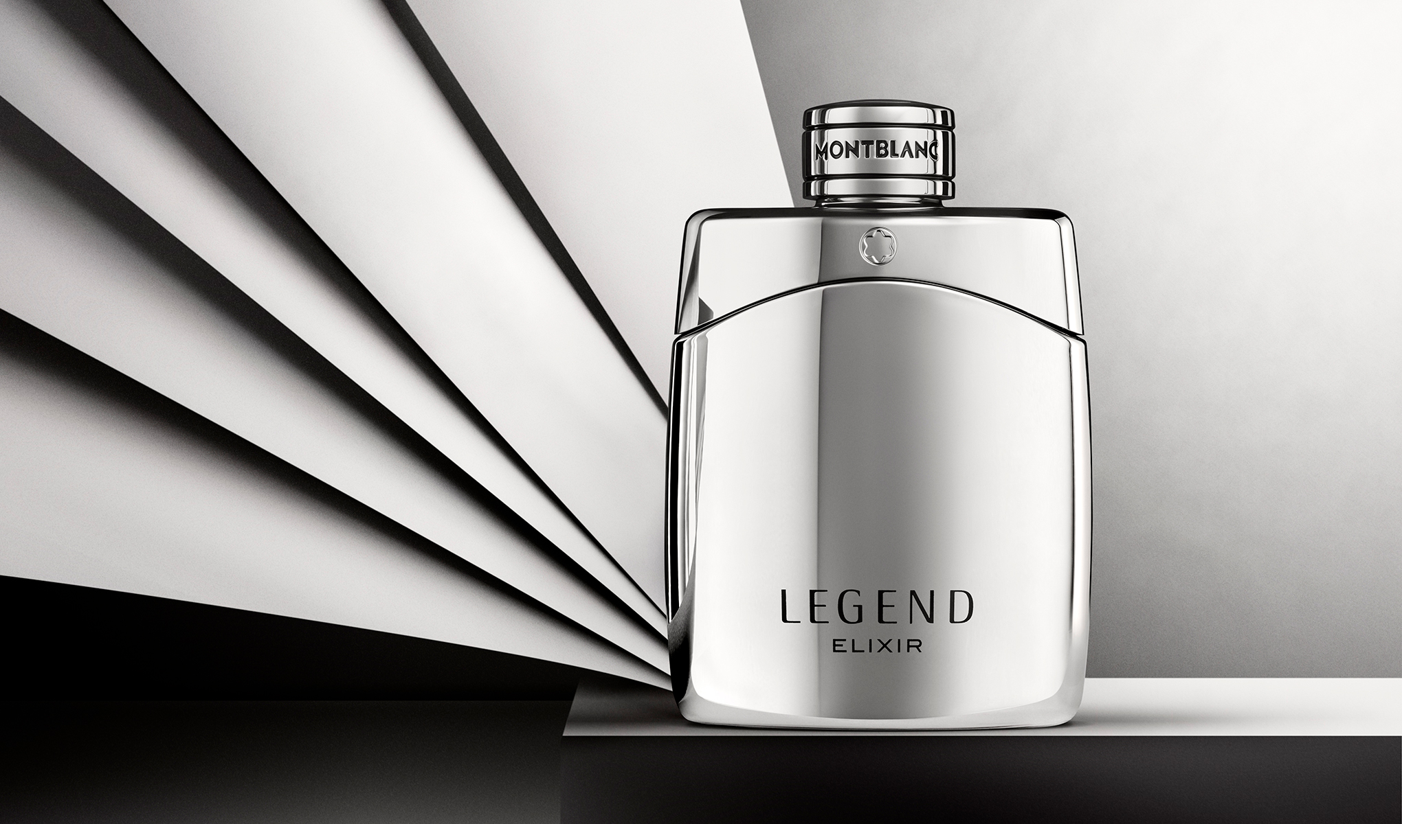Sølvfarget parfymeflaske fra Montblanc med teksten “LEGEND ELIXIR” og “MONTBLANC” på korken, plassert foran en bakgrunn med svarte og hvite grafiske linjer. Stilrent produktbilde av herreparfyme med reflekterende overflate og minimalistisk design.