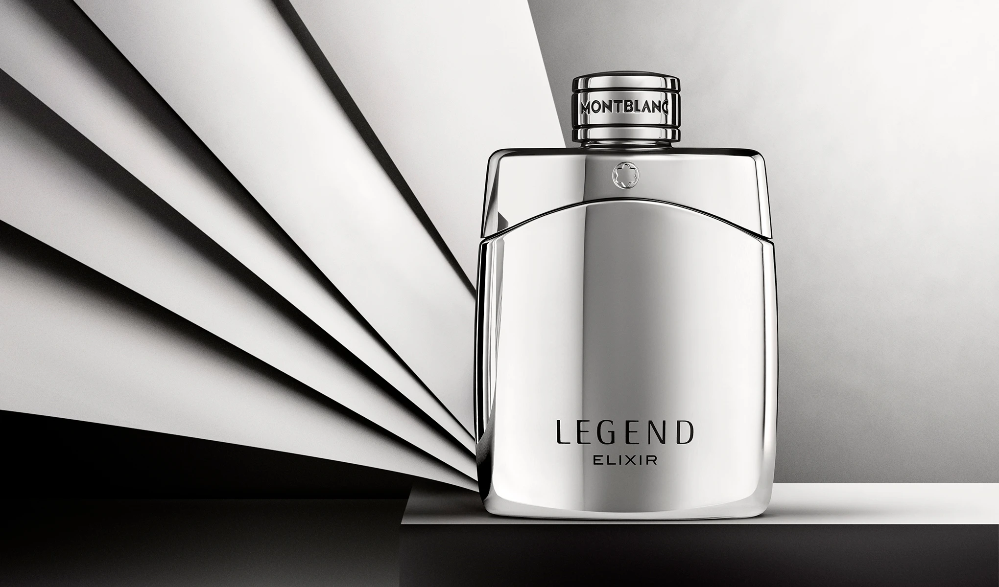 Sølvfarget parfymeflaske fra Montblanc med teksten “LEGEND ELIXIR” og “MONTBLANC” på korken, plassert foran en bakgrunn med svarte og hvite grafiske linjer. Stilrent produktbilde av herreparfyme med reflekterende overflate og minimalistisk design.