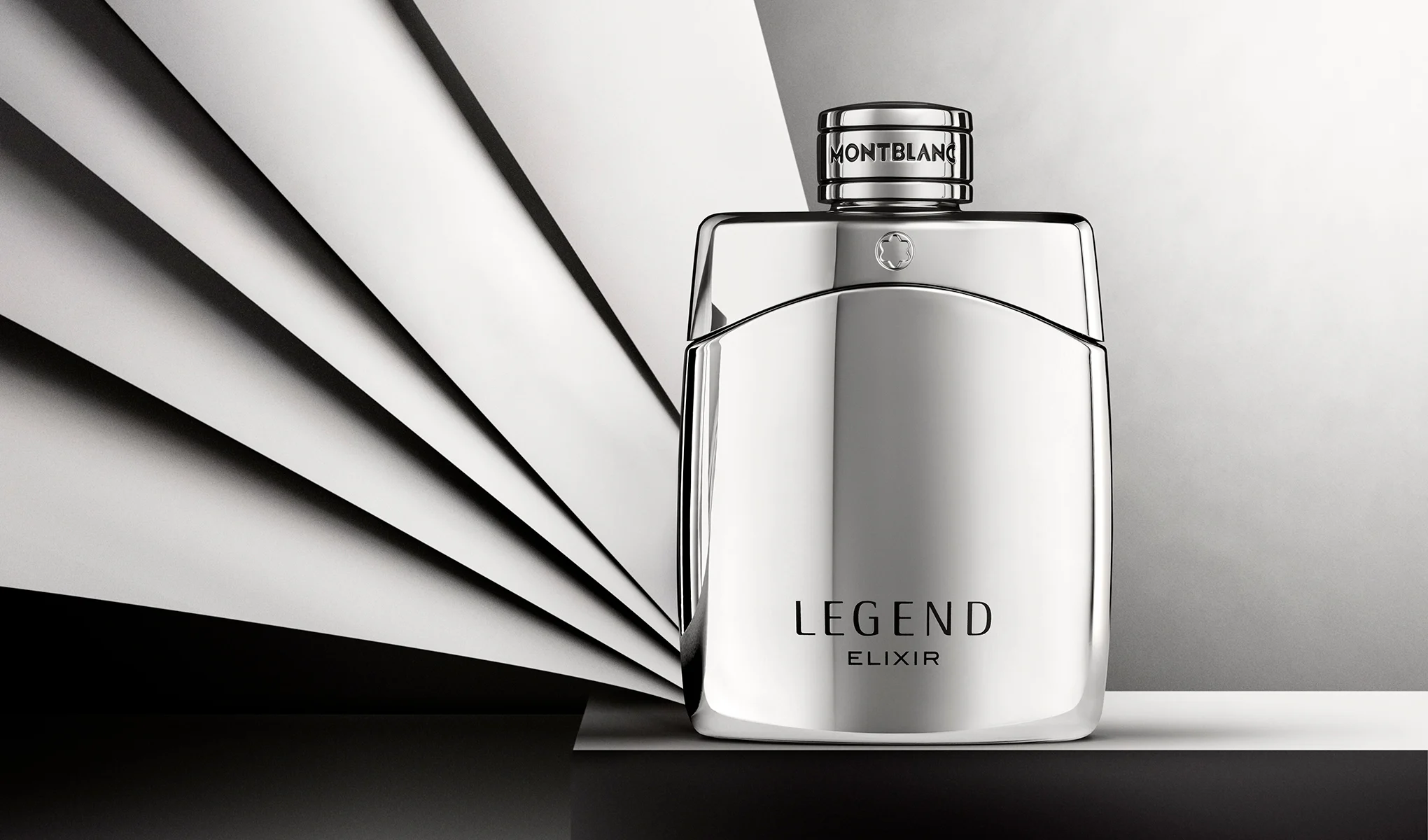 Sølvfarget parfymeflaske fra Montblanc med teksten “LEGEND ELIXIR” og “MONTBLANC” på korken, plassert foran en bakgrunn med svarte og hvite grafiske linjer. Stilrent produktbilde av herreparfyme med reflekterende overflate og minimalistisk design.
