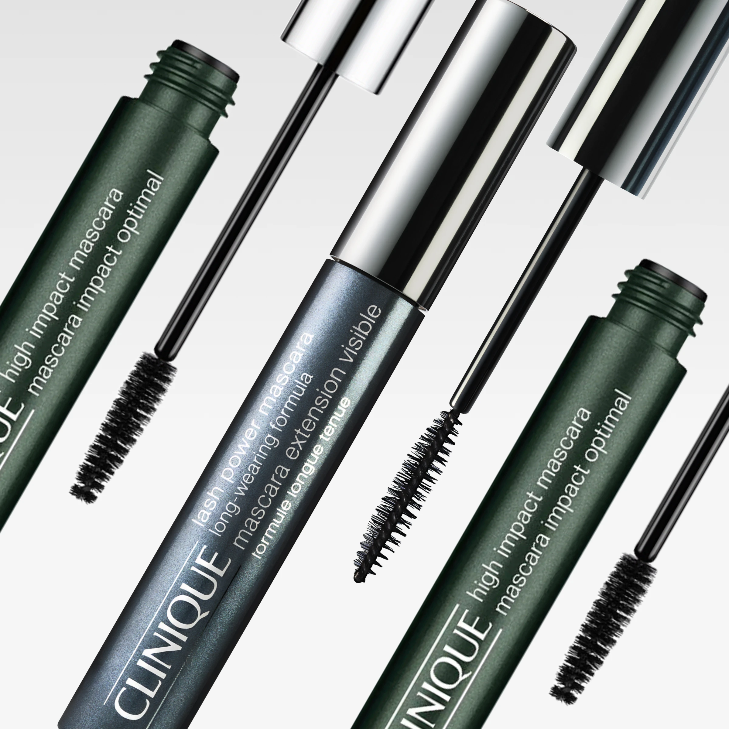 Clinique-ripsivärit vihreissä ja hopeanvärisissä pakkauksissa avoimilla mascaraharjoilla vaaleanharmaata taustaa vasten. Näkyvä teksti sisältää “high impact mascara”, “lash power mascara long-wearing formula” ja “mascara extension visible”.