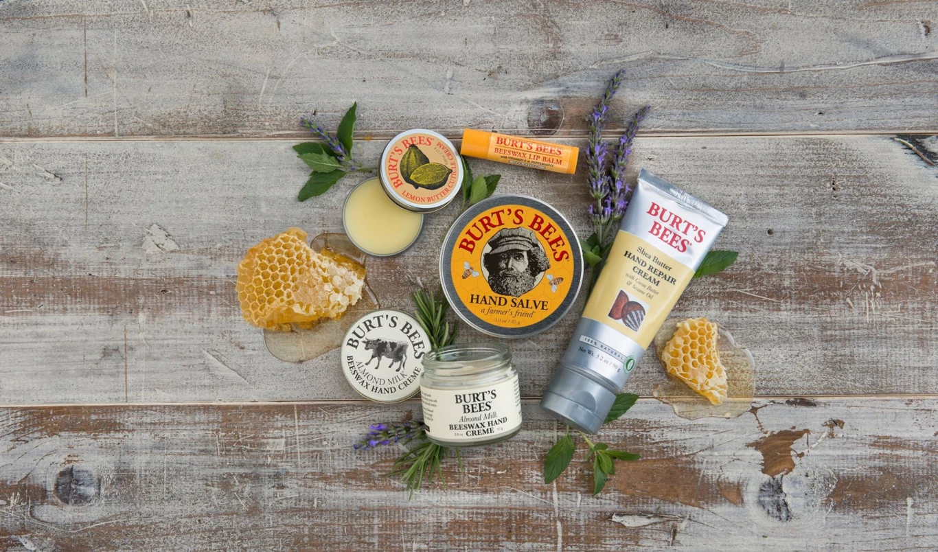 Erilaisia Burt's Bees -tuotteita, kuten käsivoidetta, huulirasvaa ja käsivoidetta, aseteltu puupinnalle yhdessä hunajakennojen ja laventelinoksaiden kanssa.