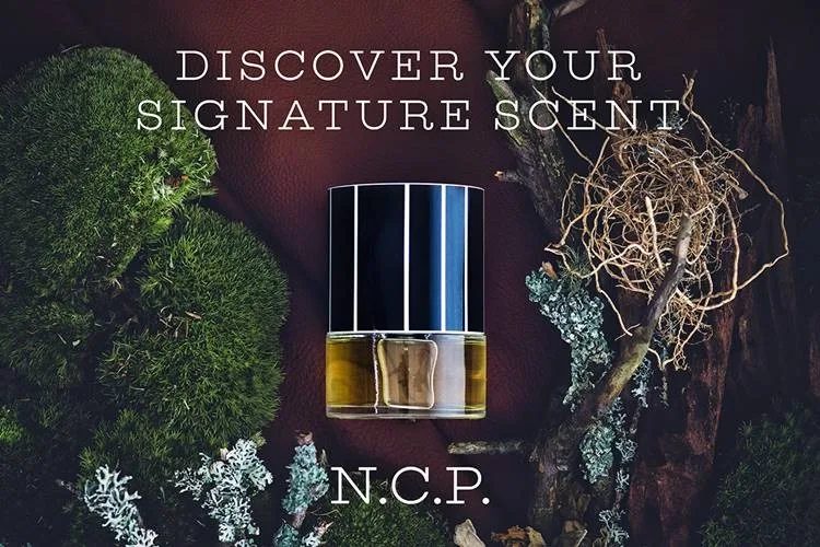 Parfymflaska från N.C.P. placerad mot en bakgrund av mossa, kvistar och bark. Texten "Discover Your Signature Scent" är skriven ovanför flaskan och "N.C.P." är skriven nedanför.