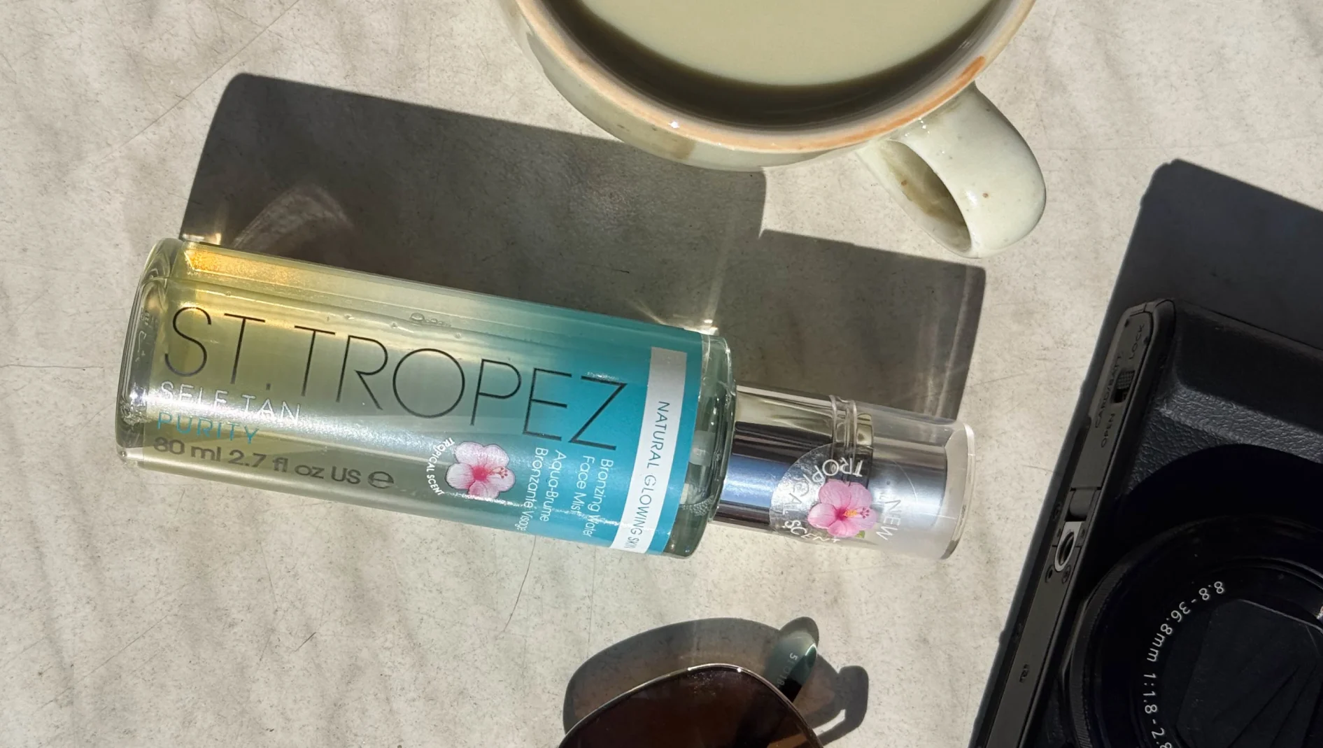 St. Tropez Self Tan Purity Bronzing Water Face Mist (80ml) luonnollisen hehkuvalle iholle, trooppinen tuoksu. Muki ja kamera vieressä.