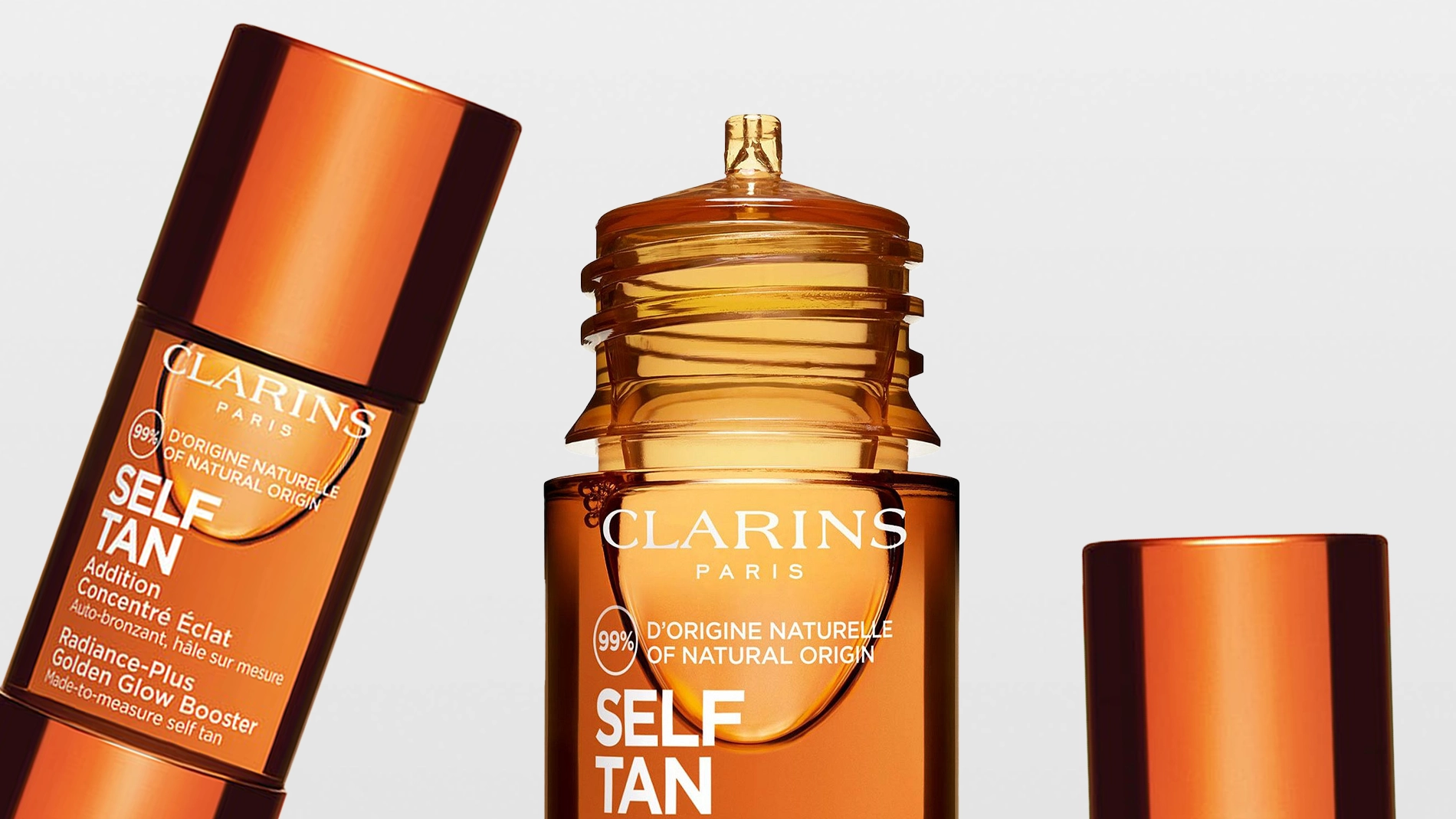 Nærbilde av bruntonede Clarins self tan-produkter med teksten “CLARINS PARIS”, “SELF TAN” og “99% D’ORIGINE NATURELLE / OF NATURAL ORIGIN” på flaskene mot lys bakgrunn. Flere emballasjer i skinnende kobberfarge viser selvbruningsprodukter for ansikt og kropp.