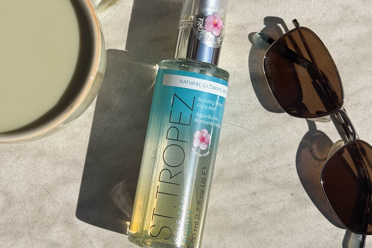 St. Tropez Self Tan Purity Bronzing Water Face Mist placerad på ett bord i solljus bredvid ett par solglasögon och en kopp.