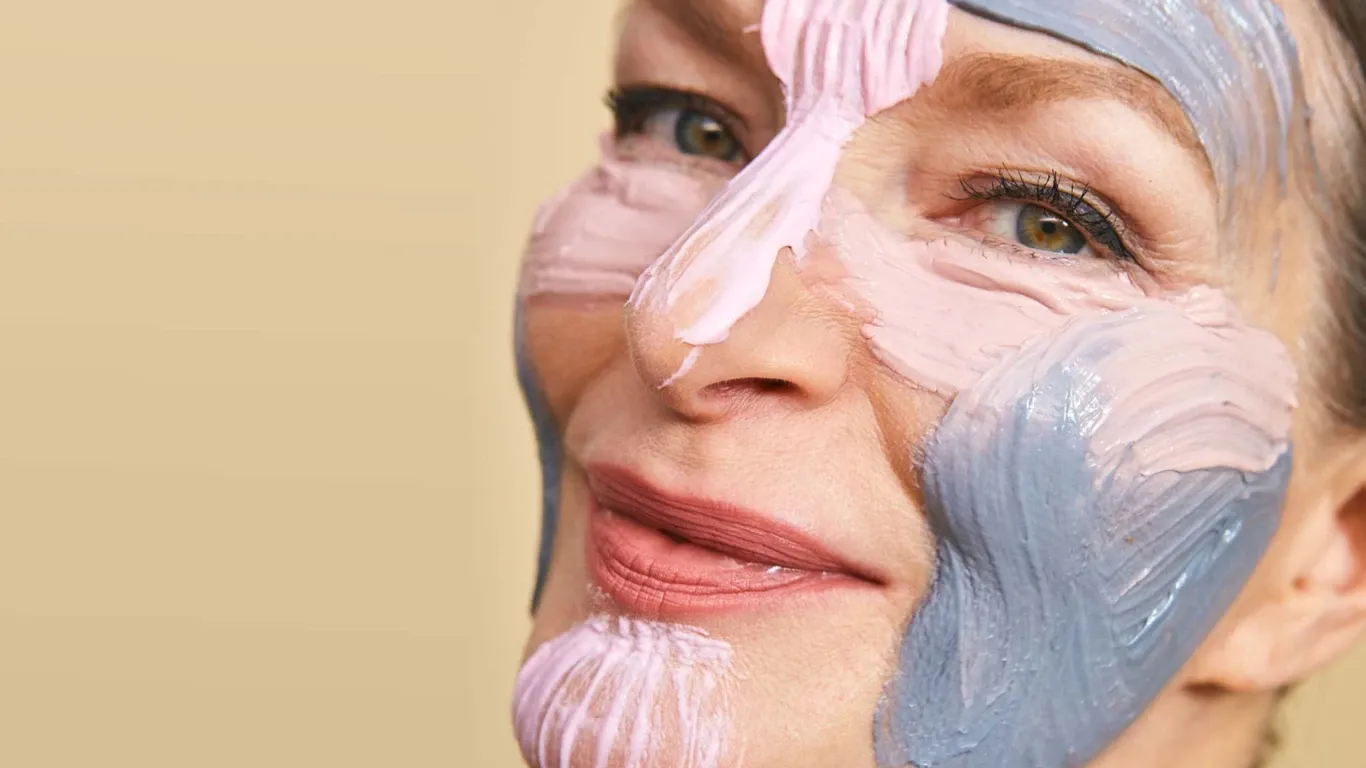 Smilende kvinne med grå og rosa gjørmemaske i ansiktet.