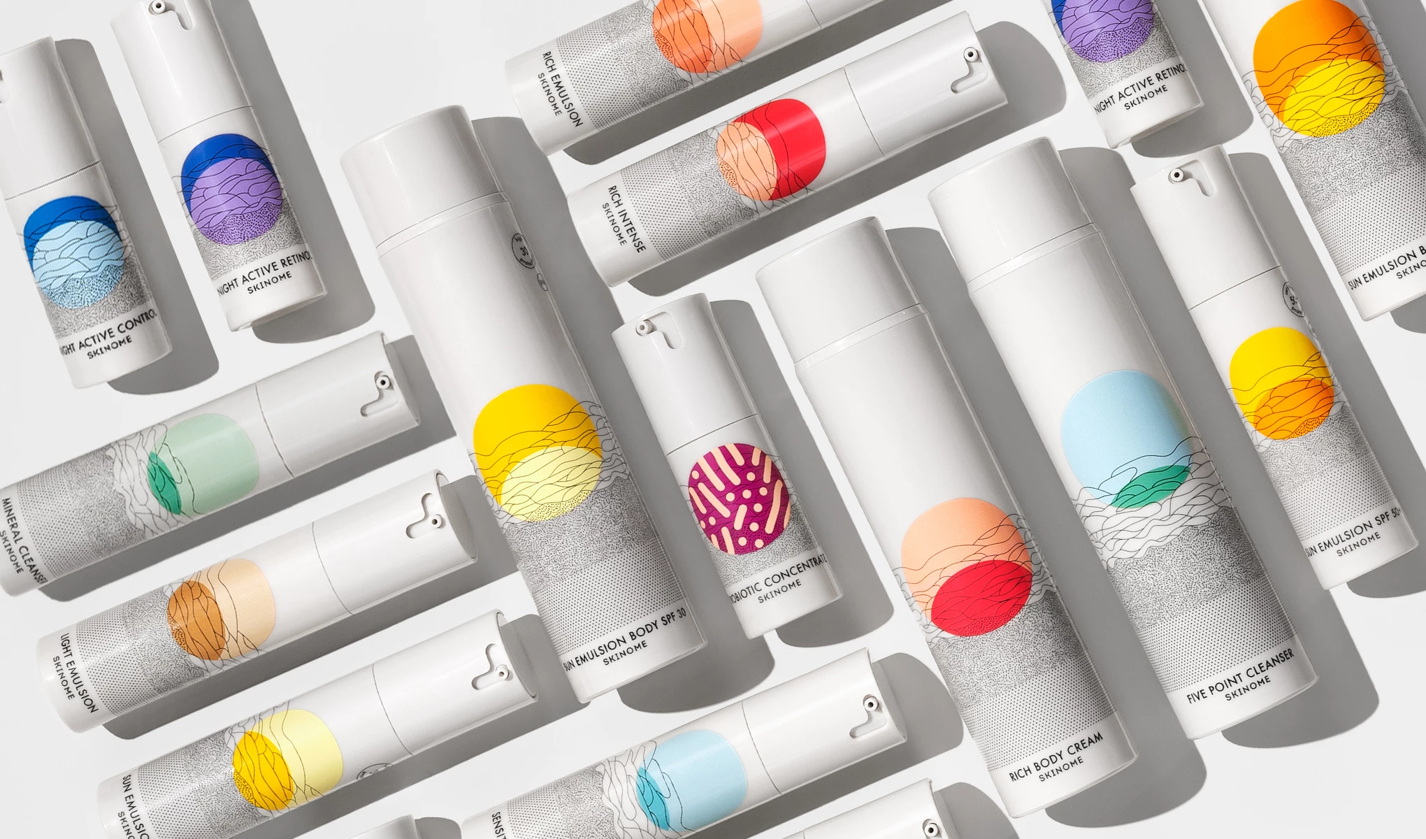 Flere hudpleieprodukter fra Skinome med hvite emballasjer og fargerike grafiske mønstre, arrangert på en lys bakgrunn.