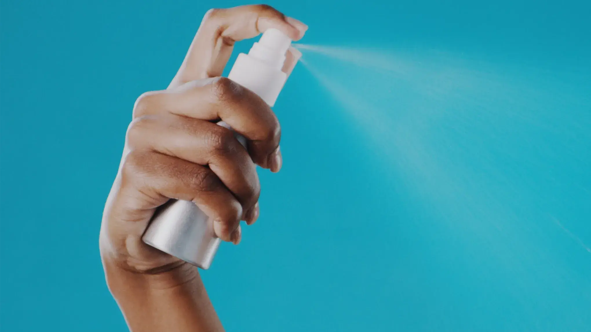 En hand som sprayar ansiktsmist mot en blå bakgrund.