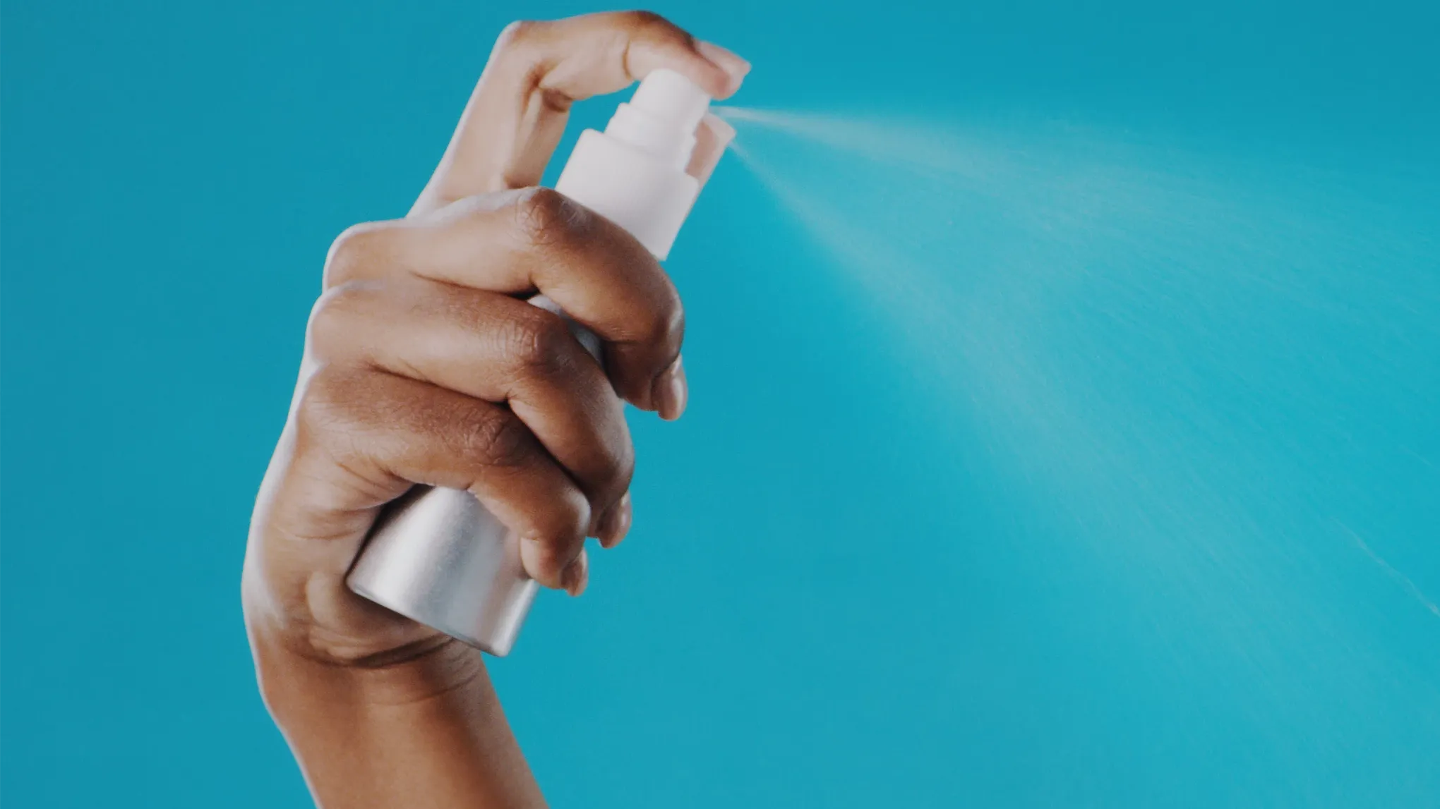 En hånd som sprayer ansiktsmist mot en blå bakgrunn.