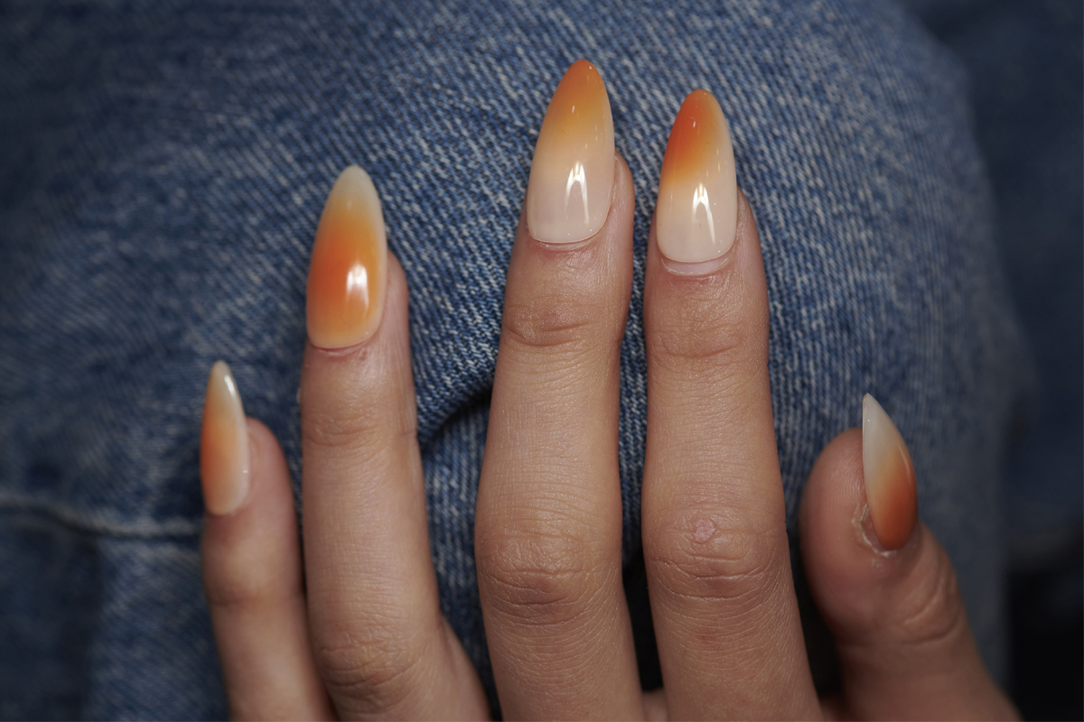 Hand mot jeans, med naglar tonade från beige till orange.