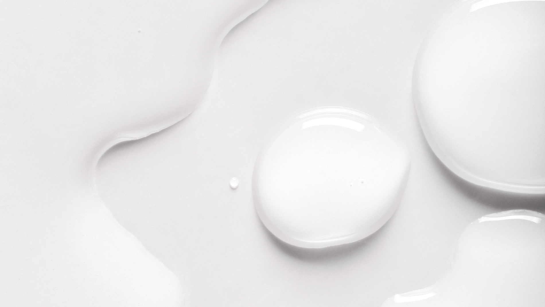 Närbild av transparent hudvårdsserum i flytande form med mjuka droppar och glansig yta mot vit bakgrund. Minimalistisk texturbild som framhäver serumets konsistens inom skincare.