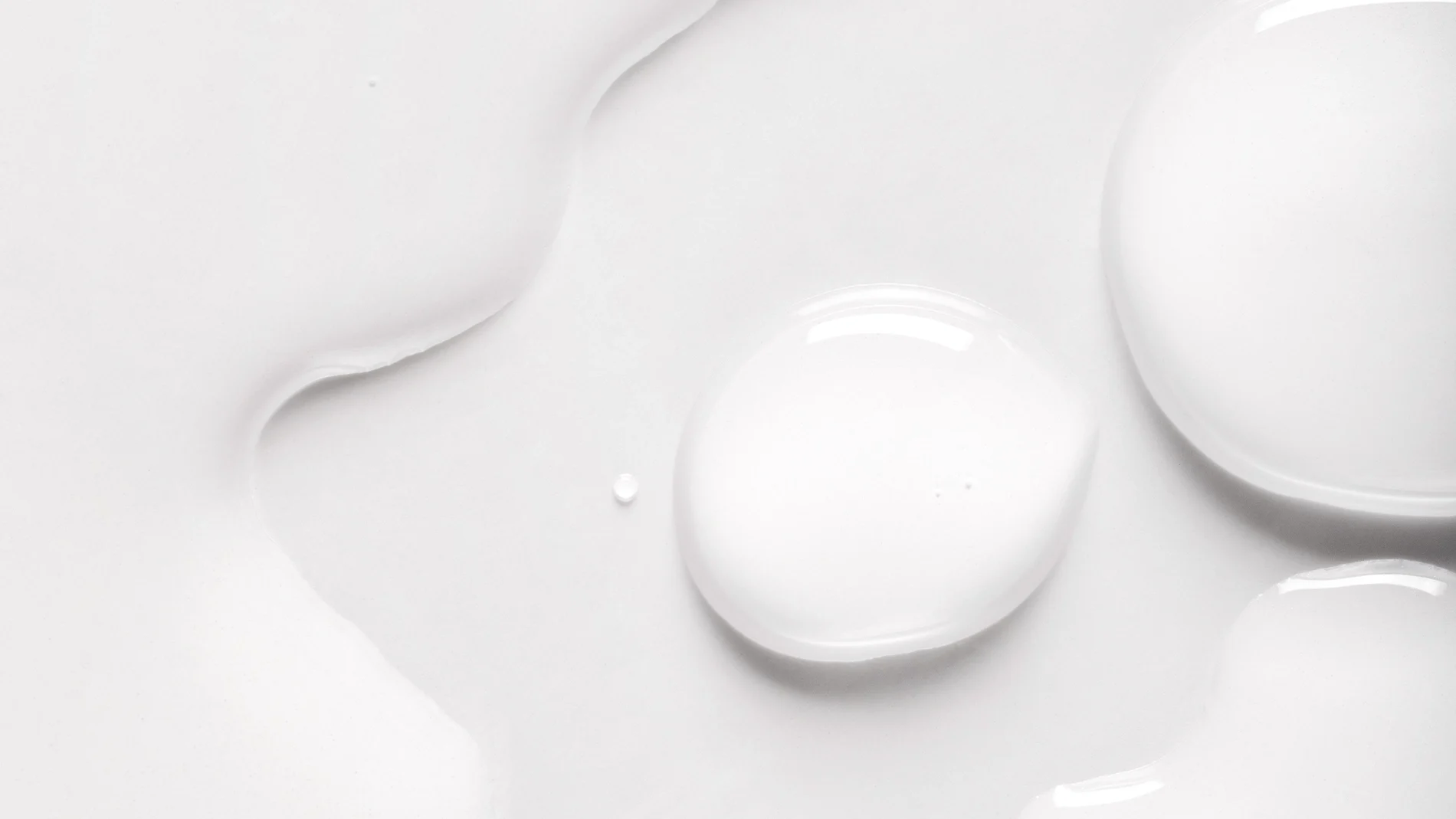 Närbild av transparent hudvårdsserum i flytande form med mjuka droppar och glansig yta mot vit bakgrund. Minimalistisk texturbild som framhäver serumets konsistens inom skincare.