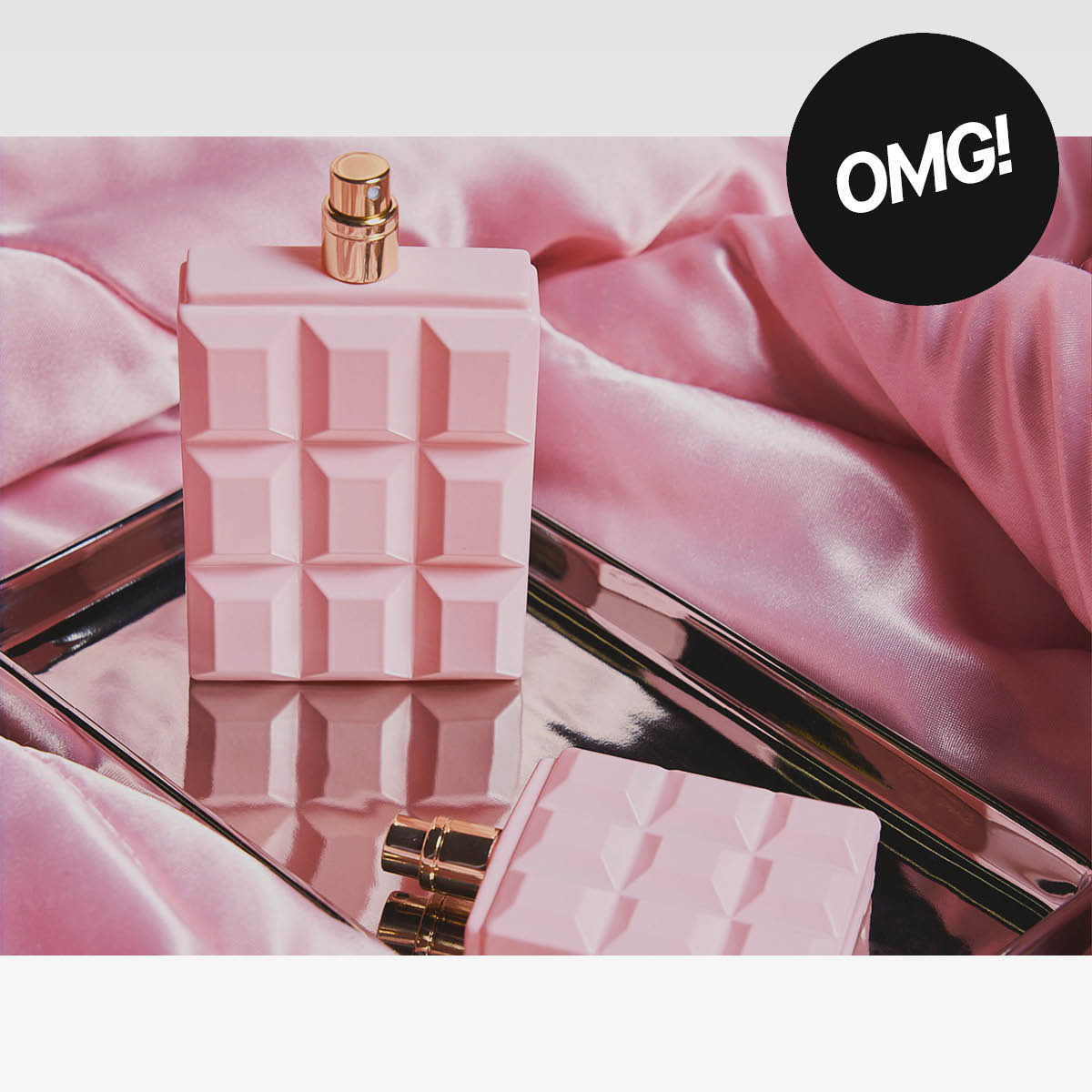 Rosa parfymflaska och ytterligare en flaska på spegelyta mot rosa tygbakgrund, med texten ”OMG!”.