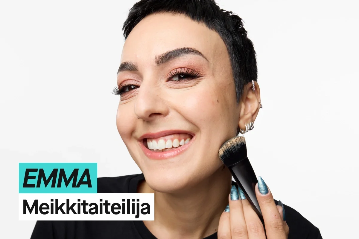 Henkilö, jolla on lyhyet mustat hiukset, levittää meikkiä siveltimellä poskelle vaaleanharmaata taustaa vasten ja käyttää mustaa KICKS-paitaa. Turkoosi ja valkoinen teksti näyttävät “EMMA” ja “Makeupartist”.