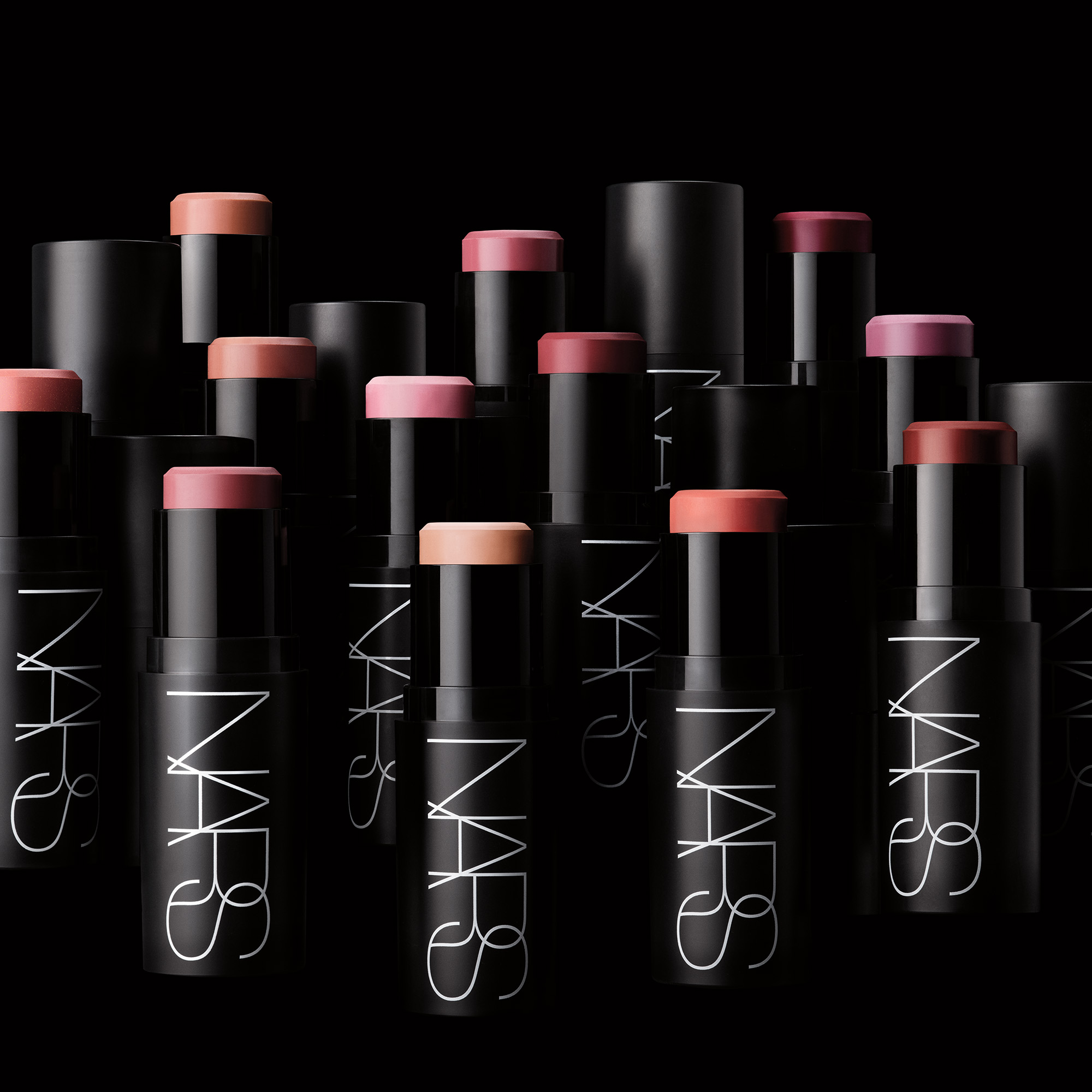 Flere NARS cream blush-sticks i rosa, fersken, nude og bærtoner er arrangert mot svart bakgrunn. De svarte hylsene har den hvite logoen “NARS” og fremhever kremrouge i ulike nyanser.