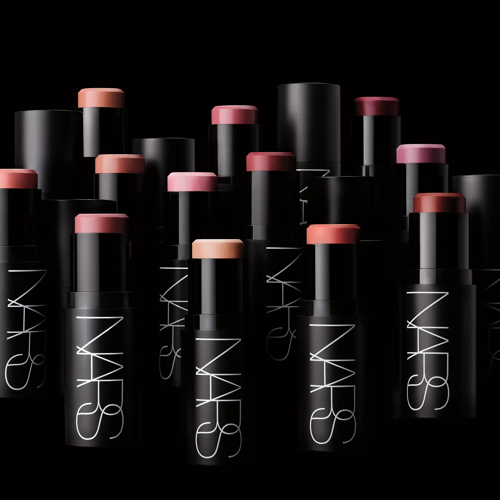 Flere NARS cream blush-sticks i rosa, fersken, nude og bærtoner er arrangert mot svart bakgrunn. De svarte hylsene har den hvite logoen “NARS” og fremhever kremrouge i ulike nyanser.