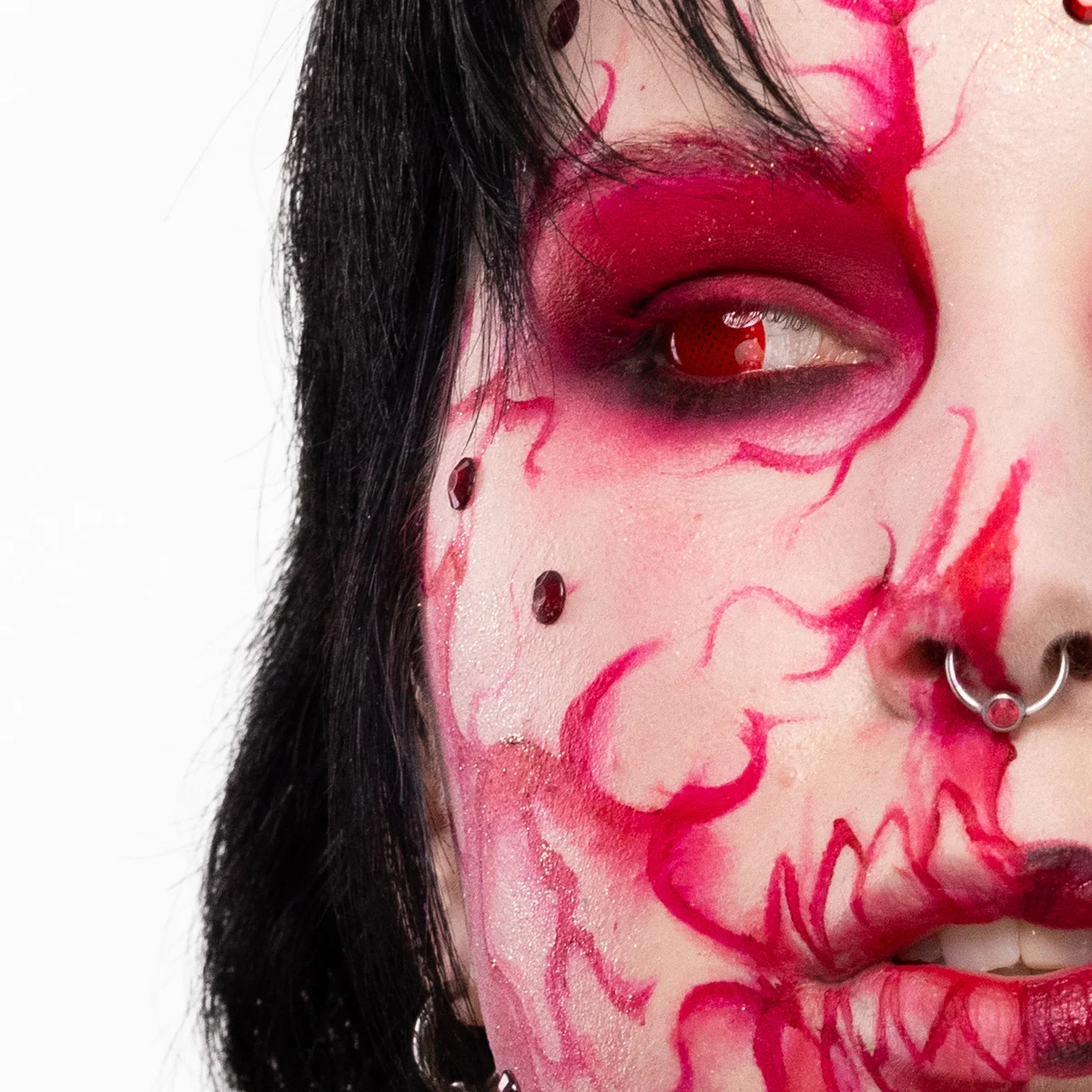 Närbild av dramatisk halloweenmakeup runt ögonen, med intensiv röd och rosa ögonskugga, konstnärliga målade ådror och dekorerande röda stenar över båda ögonlocken samt en kontrastlins som förstärker looken.
