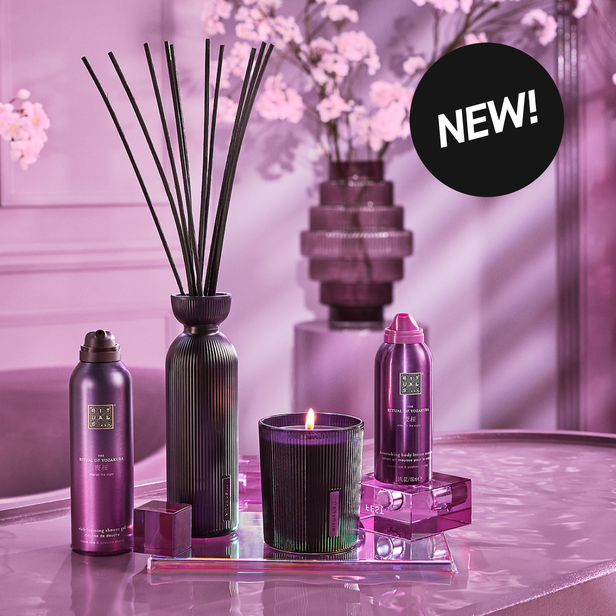 Lillafarget produktoppsett med duftpinner, tent lys og to kroppspleieprodukter. «NEW!» i øvre hjørne.