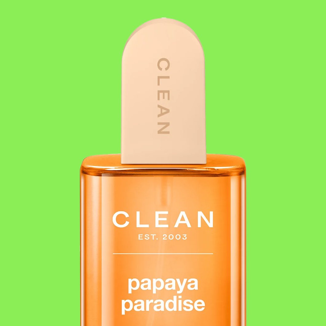 Parfymflaska i orange med texten “CLEAN EST. 2003 papaya paradise” och kork märkt “CLEAN” mot grön bakgrund.